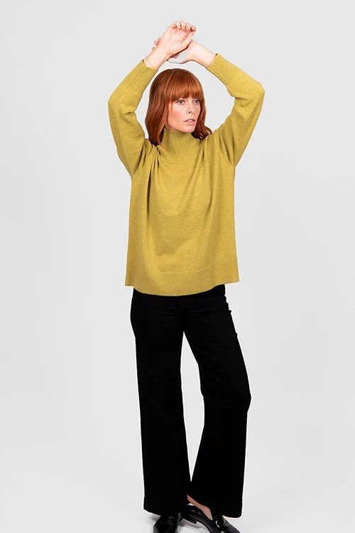 Woman wearing the Citrine colour variant in the Bridge & Lord | Boxy Rib Funnel Neck Pullover made from Merino wool and cashmere. Her arms are up which shows it's loose-fitting style