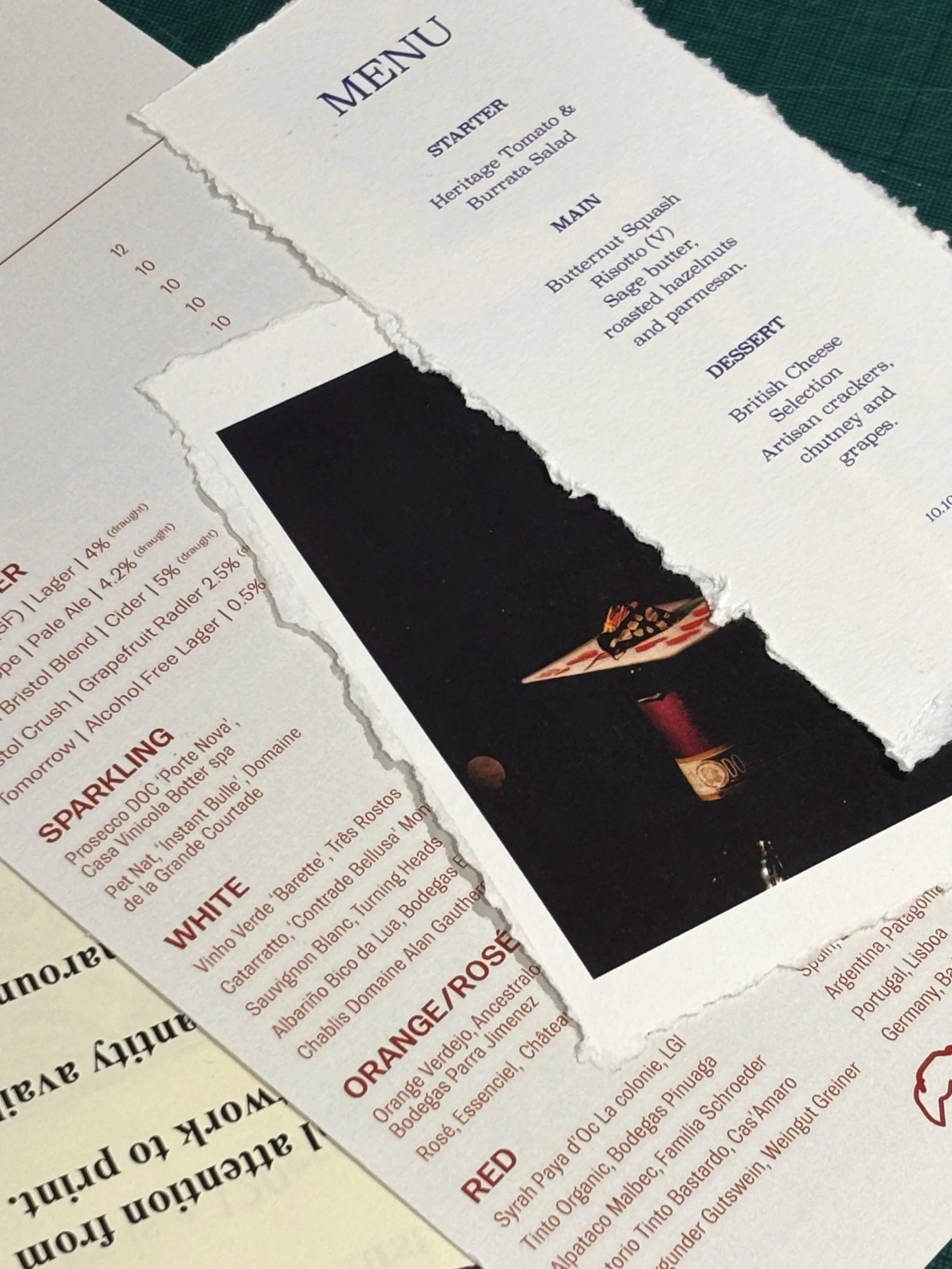 Close-up of a torn paper menu with main courses and desserts listed, and part of a wine list underneath.
