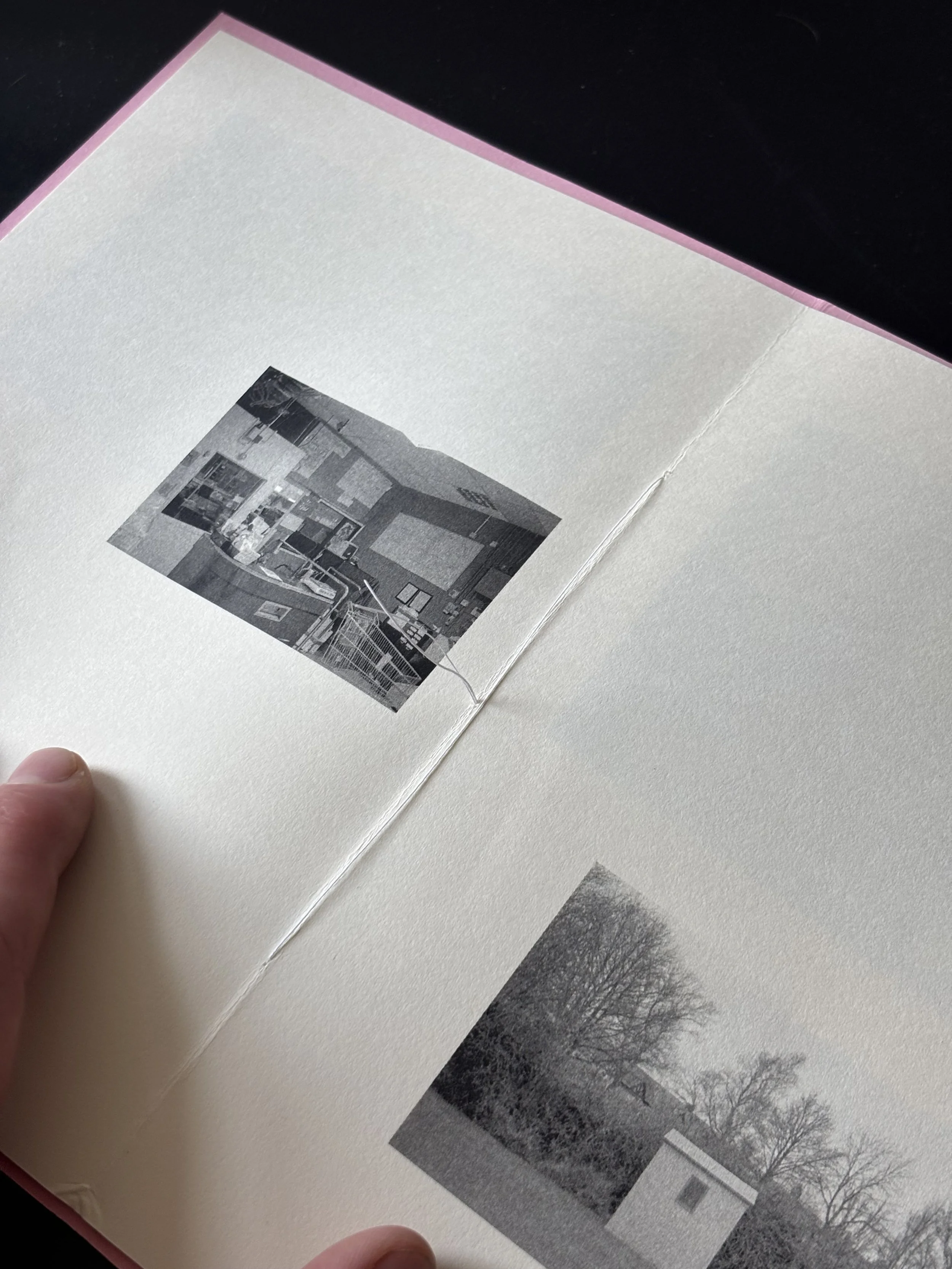 Open photo book showing black and white images of outdoor scenes, including trees, a yard, and a building.