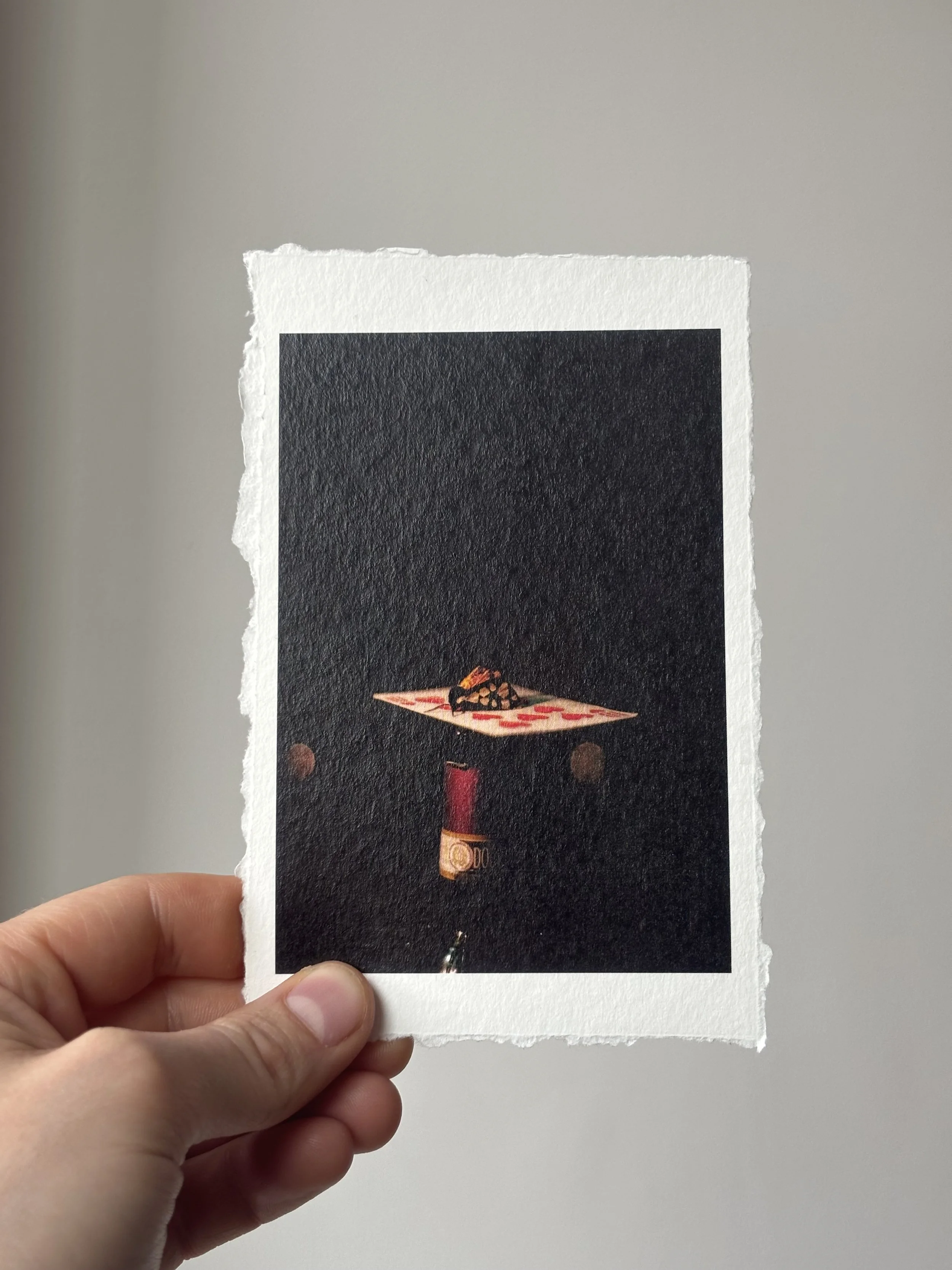 A piece of paper with a printed image of a moth on playing card atop a n open wine bottle. The paper has torn edges and is held by a person's hand against a plain gray wall.