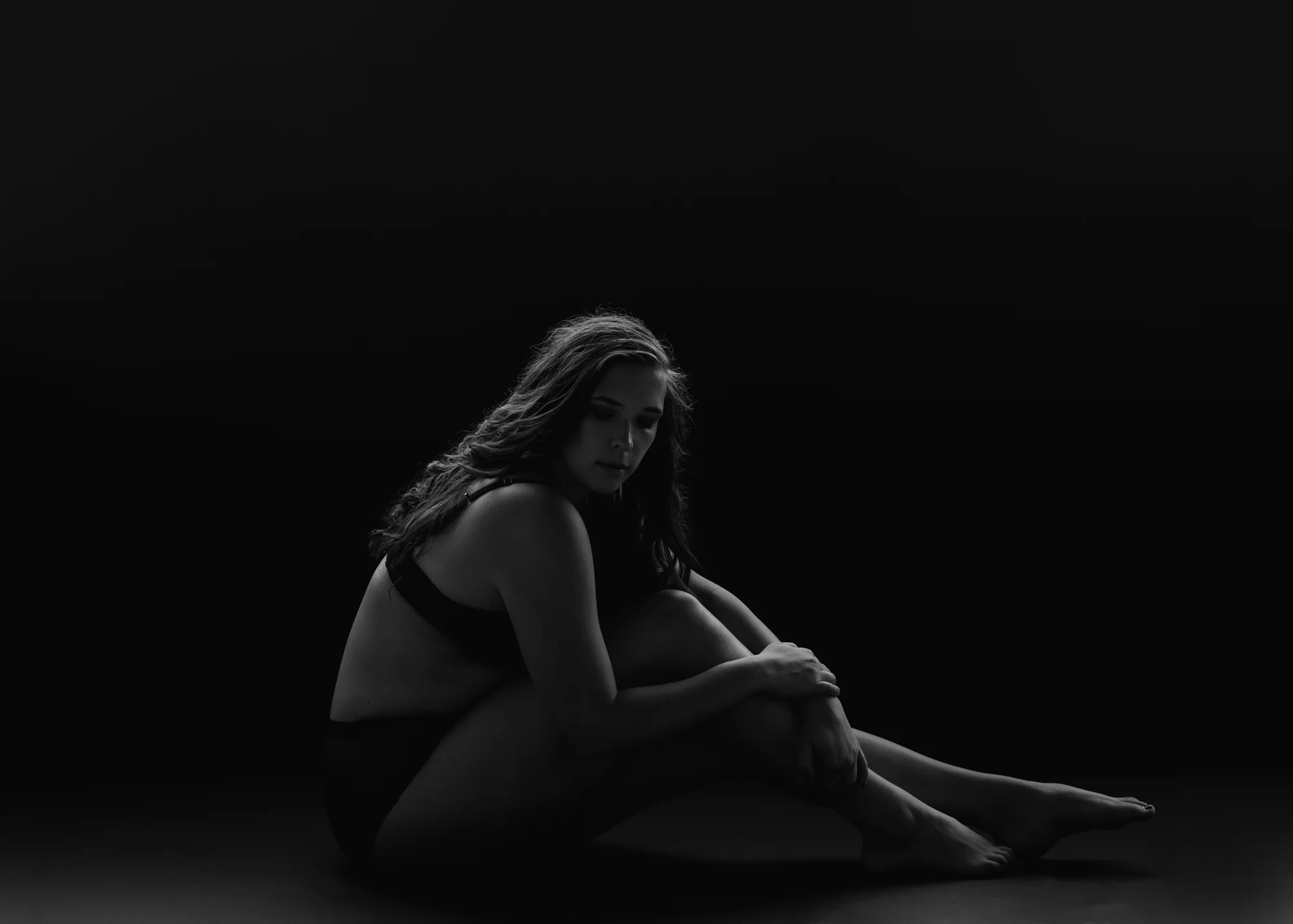 woman sitting in black bra and panties with arms hugging knees into chest
