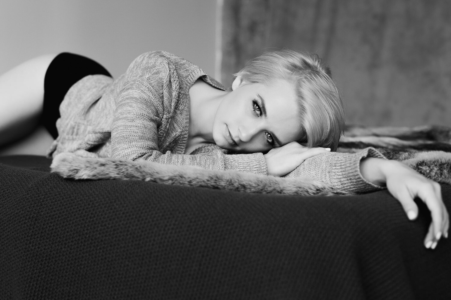 blonde woman with short hair lying on stomach on bed