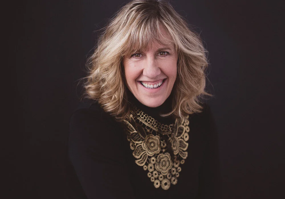 60 year old woman smiling against a dark backdrop