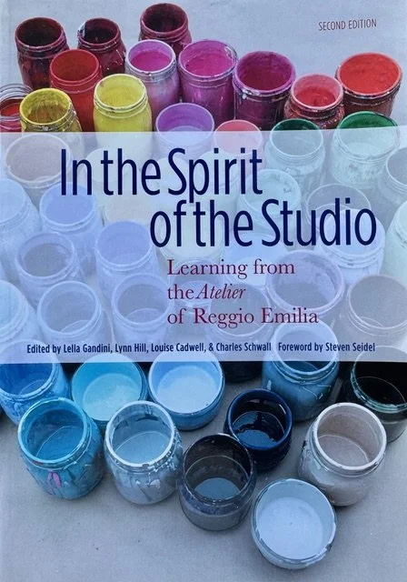 Book titled 'In the Spirit of the Studio: Learning from the Atelier of Reggio Emilia,' with a background of colorful open paint jars arranged in rows.