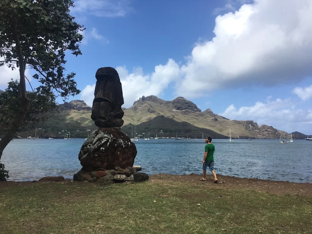 Clif walking through a tiki park in Taiohae with traditional stone tiki carvings-- and the large number of sailboats in the bay!