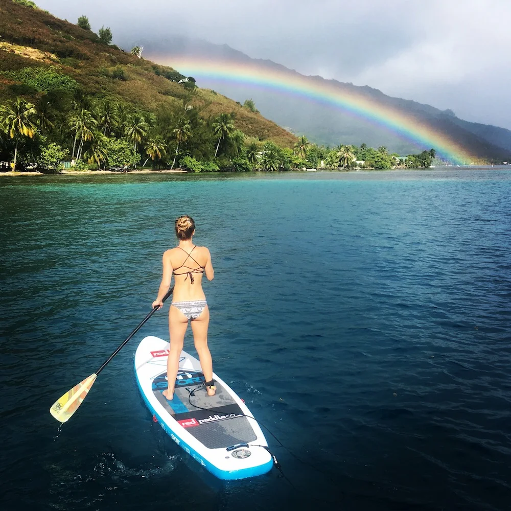 Connie paddle boarding into a rainbow on the island of Moorea.