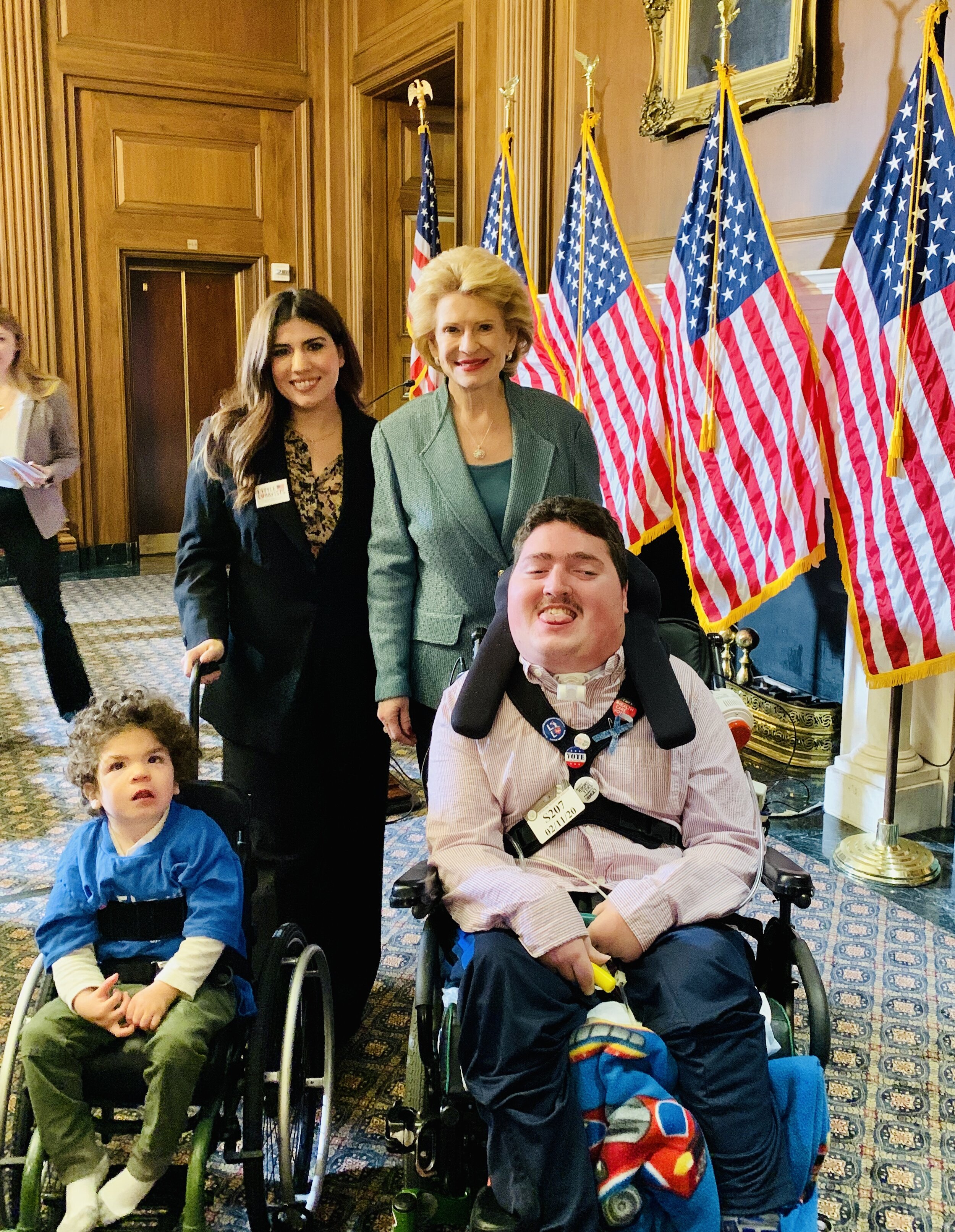  Little Lobbyists members pose with a U.S. Senator after a press conference, with U.S. flags in the background. 