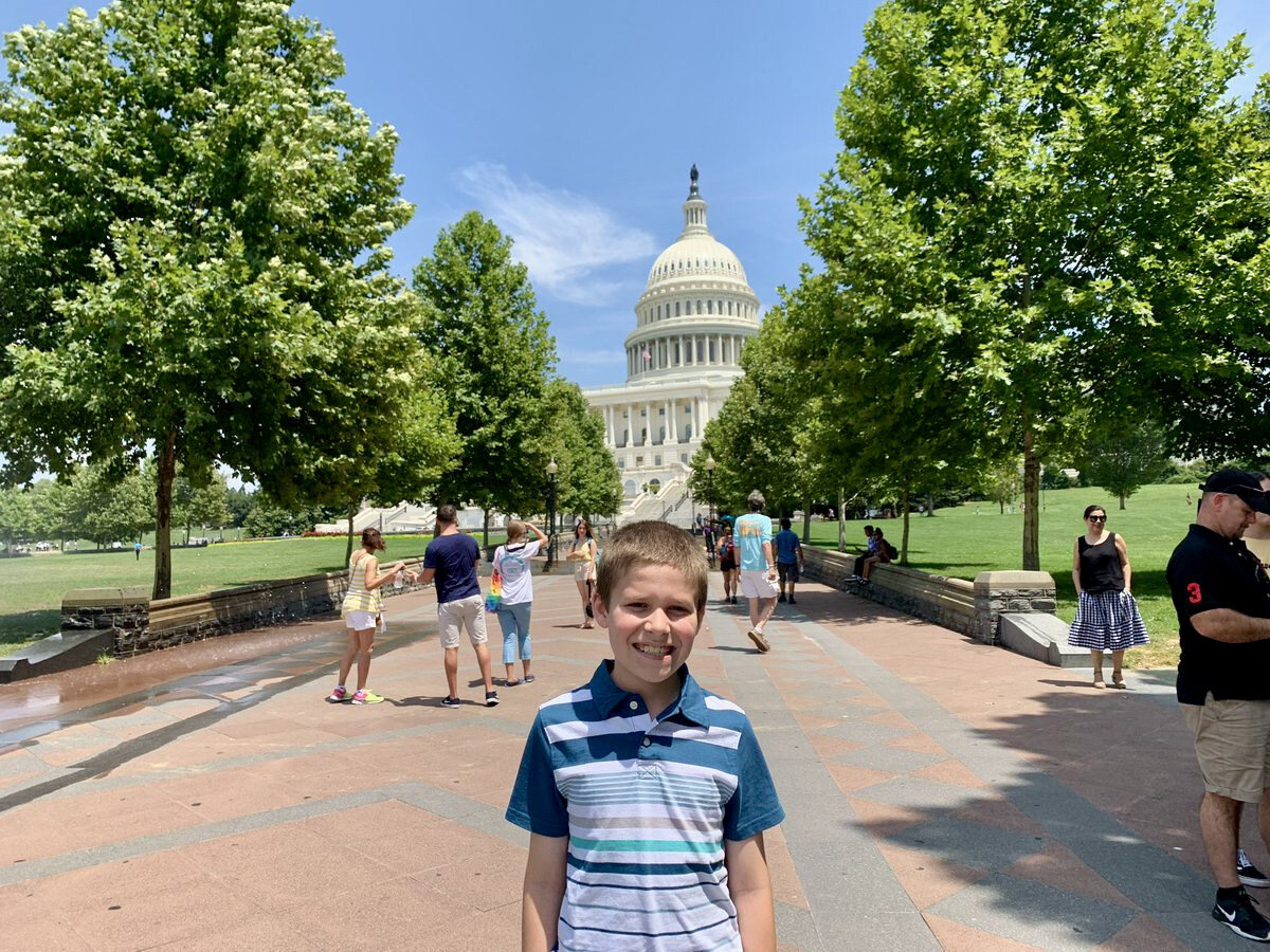  A young boy poses on a tree-lined street near the U.S. Capitol, with the Capitol dome in the background. 