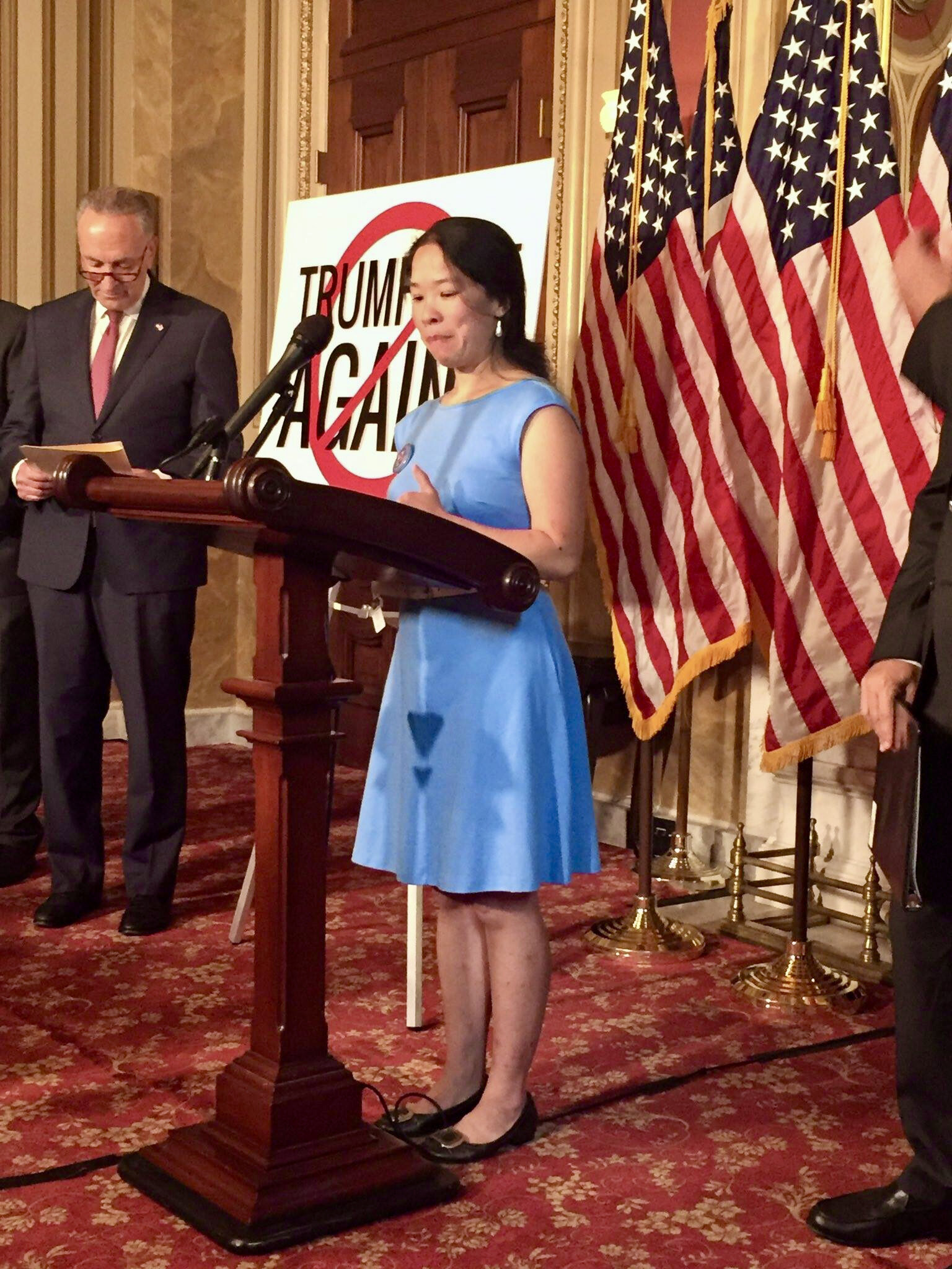  A founder of Little Lobbyists delivers remarks from a podium in the Capitol building. Flags are in the background. 