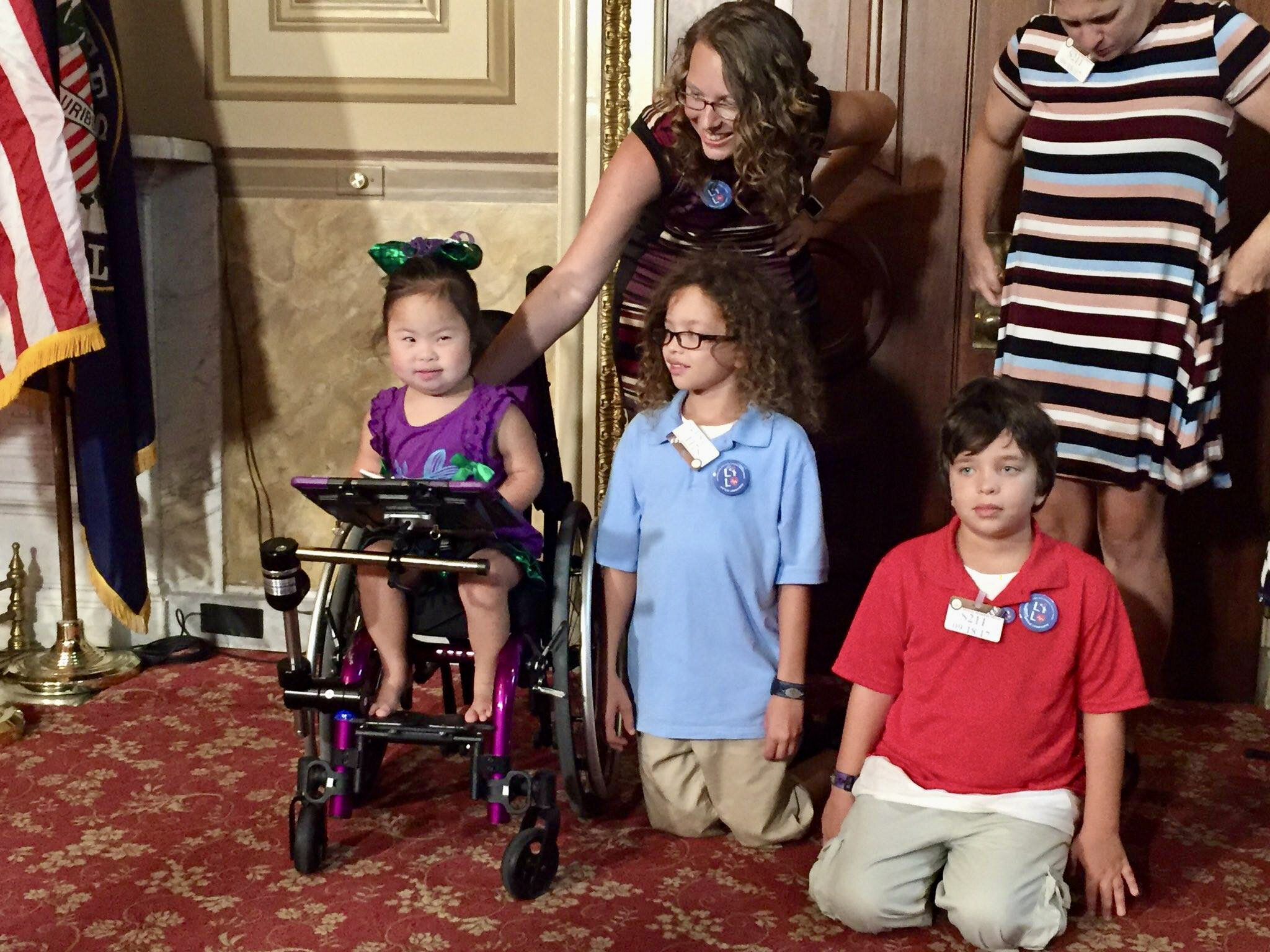 Little Lobbyists families pose during a press conference, sitting by decorative doors to the room.