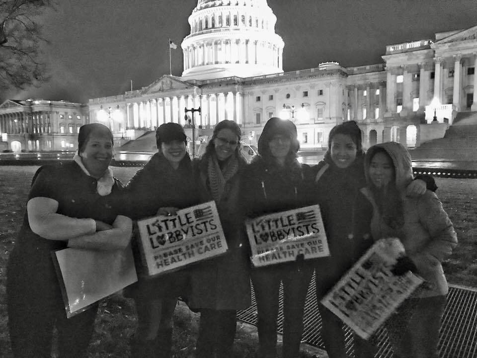  In a black and white photograph, several Little Lobbyists moms pose in front of the U.S. Capitol, during the early days of the efforts to save the Affordable Care Act. 