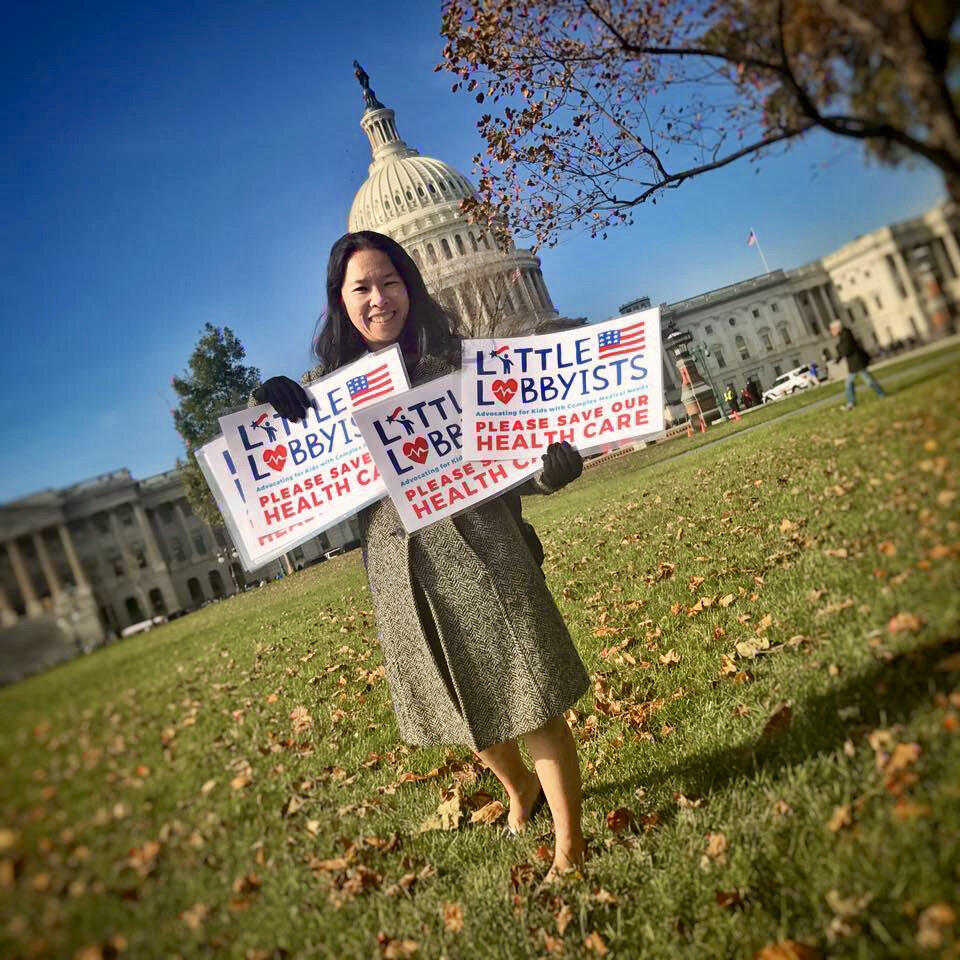  A founder of Little Lobbyists holds multiple LL signs with the LL logo in front of the U.S. Capitol on a beautiful autumn day. 