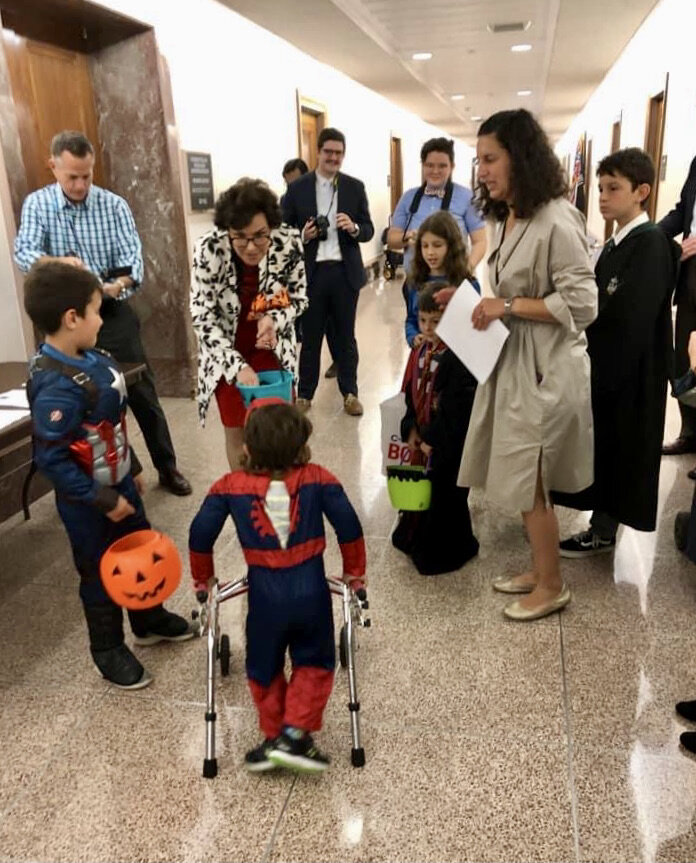  A group of Little Lobbyists in Halloween costumes speak in a hallway of a congressional office building with a legislator. 