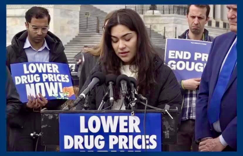  A young woman representing Little Lobbyists speaks at a podium marked with a “Lower Drug Prices” sign outside in front of the U.S. Capitol. 