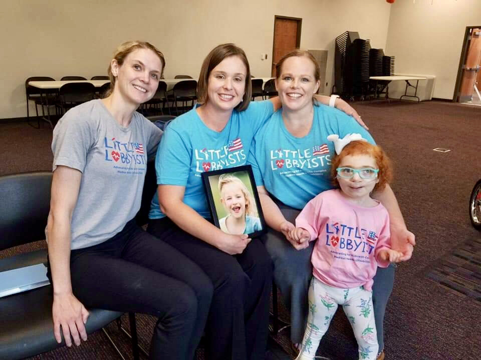  A group of Little Lobbyists families in Tennessee pose in a conference room. They wear brightly colored t-shirts with the LL logo. 