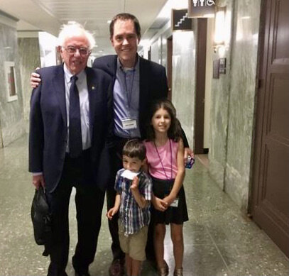  In a marble-lined hallway of a congressional office building, a dad and his kids pose with a U.S. Senator. 