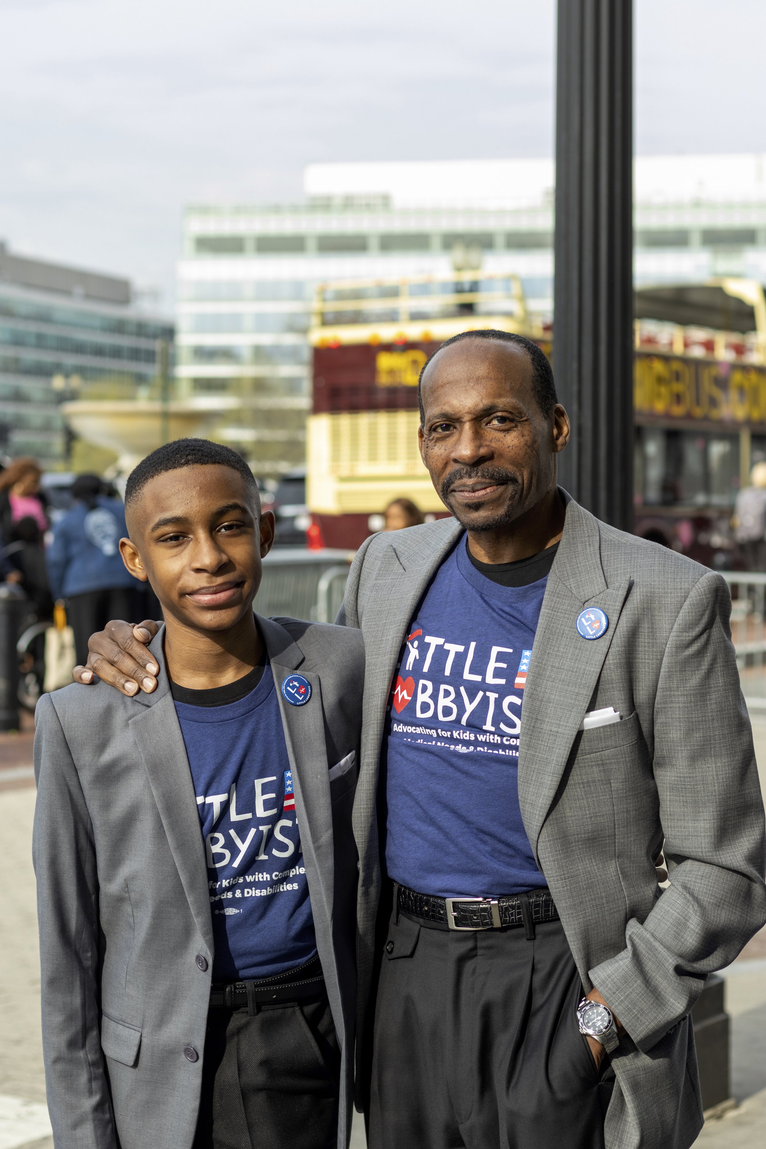  Isra'El &amp; Rico pose outside Union Station. They wear gray suit jackets with LL pins on the lapel and LL t-shirts underneath. Both have close-cropped, tightly curled dark hair. Rico has a mustache. 