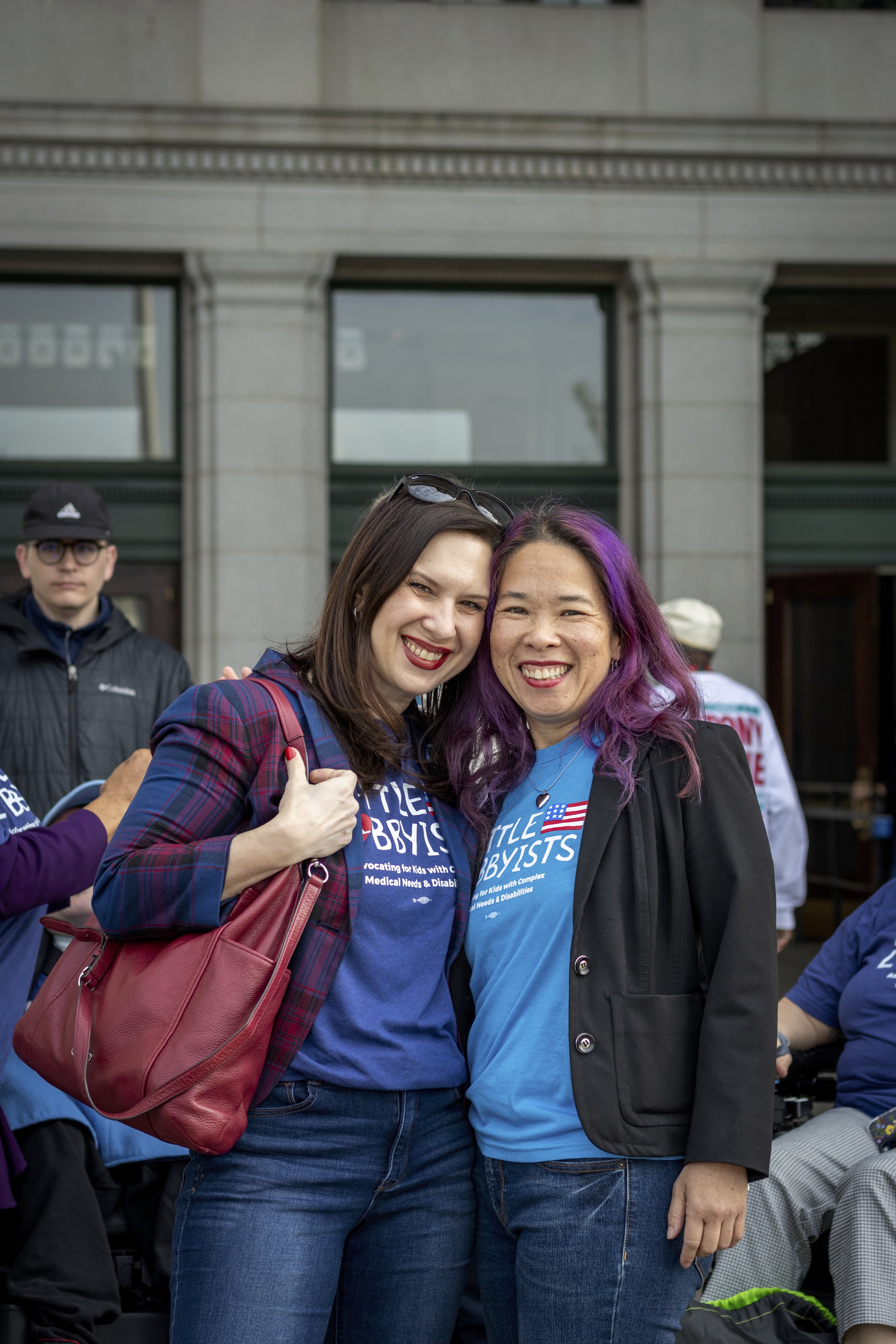  Laura and Elena pose outside the station. Laura has a large red bag over her shoulder. Elena has bright magenta streaks in her dark hair. 