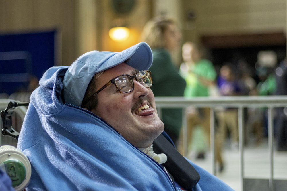  Rob, wearing his light blue wheelchair cape and a matching LL baseball hat, smiles as he waits for the rally to begin. 