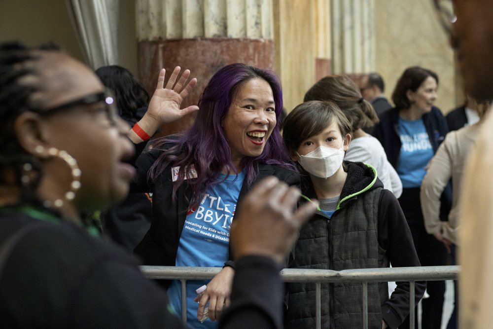  Elena and her son Khalil wave from behind a metal barrier just outside the ADA section. Khalil is wearing an N95 mask. 