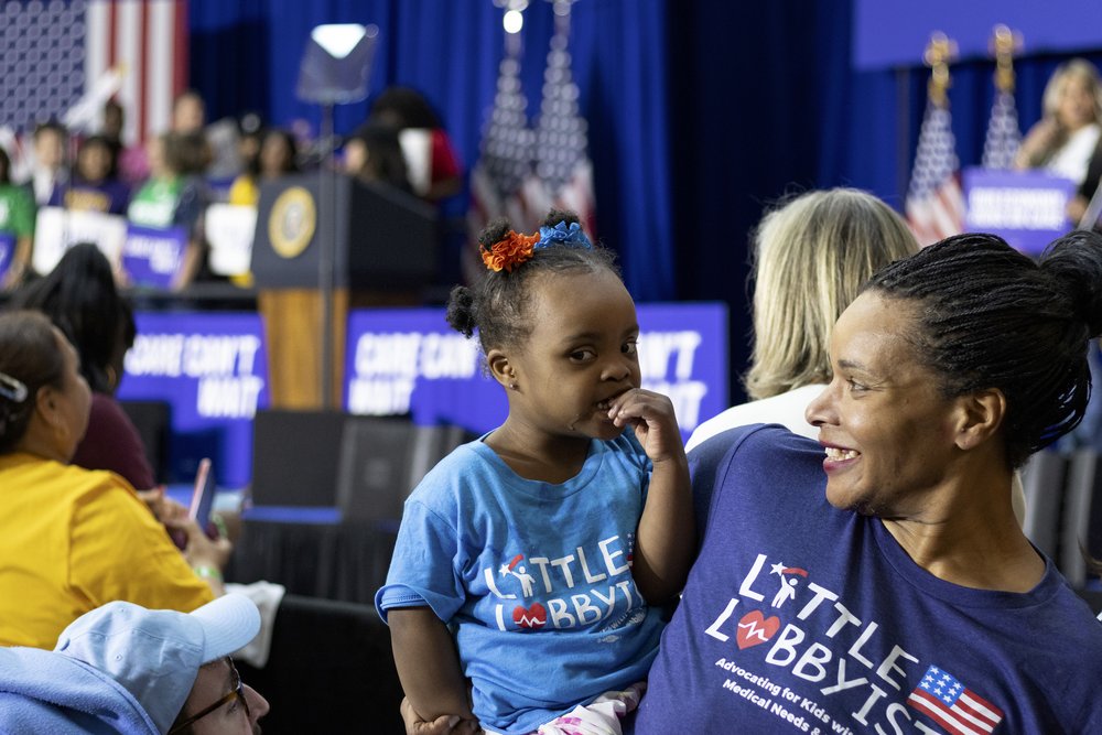  Danielle, who has elaborate cornrows and is wearing her Little Lobbyists royal blue shirt (as are all our members), holds her toddler daughter Destiny. They are looking at each other and smiling. 