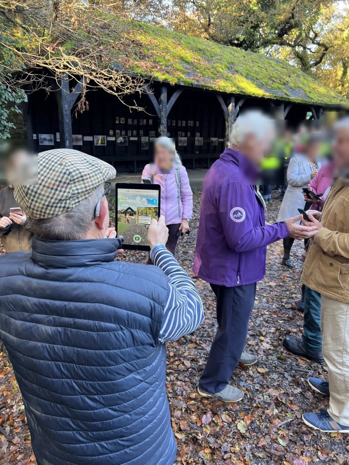 Visitor holding up a tablet showing the Burnham Beeches AR reconstruction at the Seven Ways Plain board