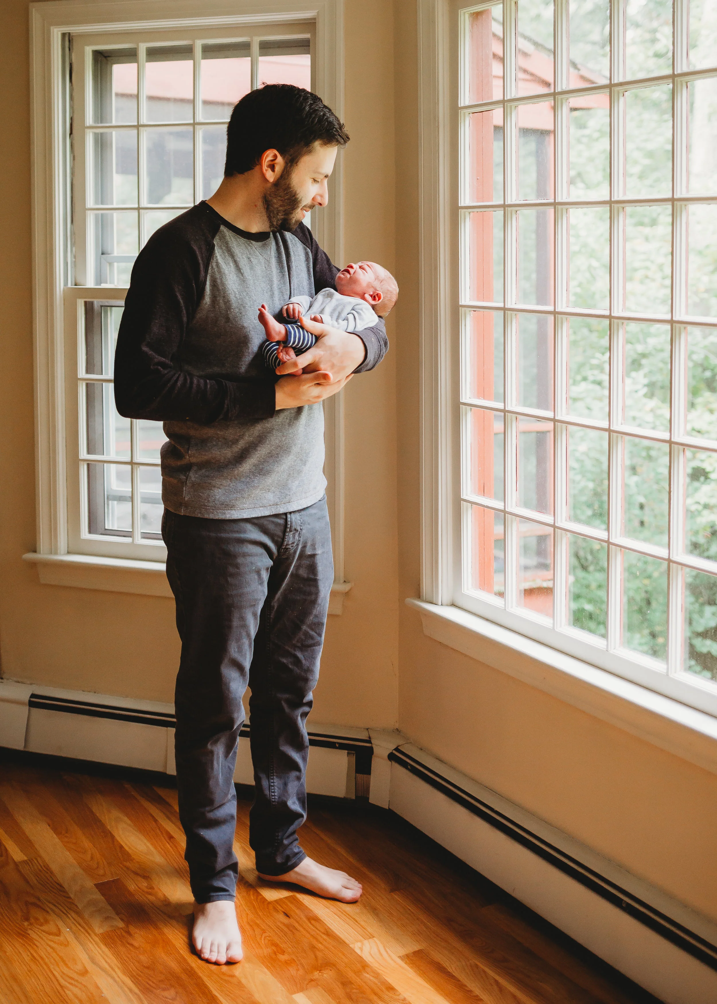Dad holding newborn near windows. Sudbury newborn photography / Boston family photographer / natural light / lifestyle