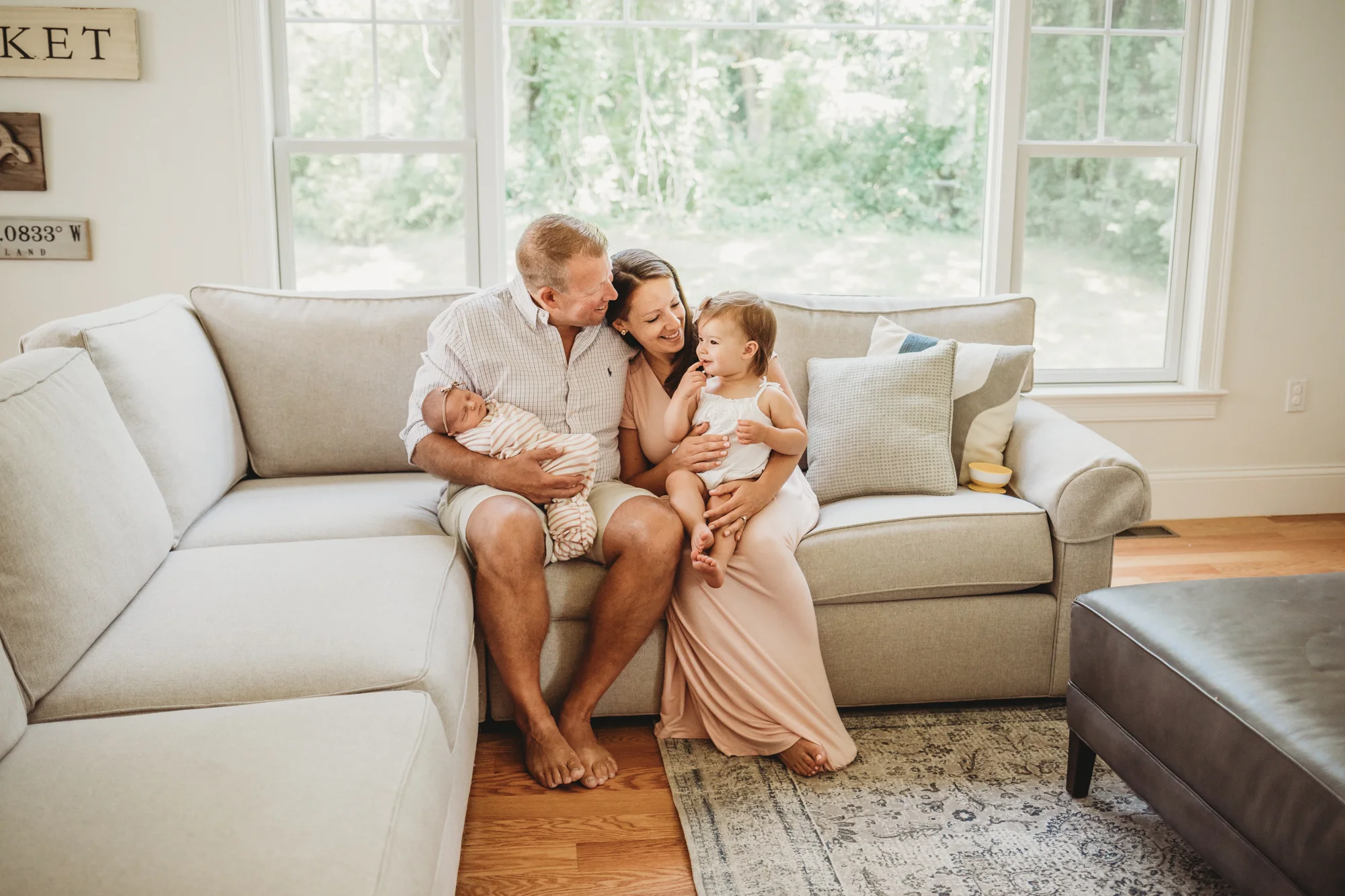 Mom and dad on the sofa with their 18-month and newborn daughters. Wayland, Massachusetts in-home newborn photography session. Lifestyle newborn photography.