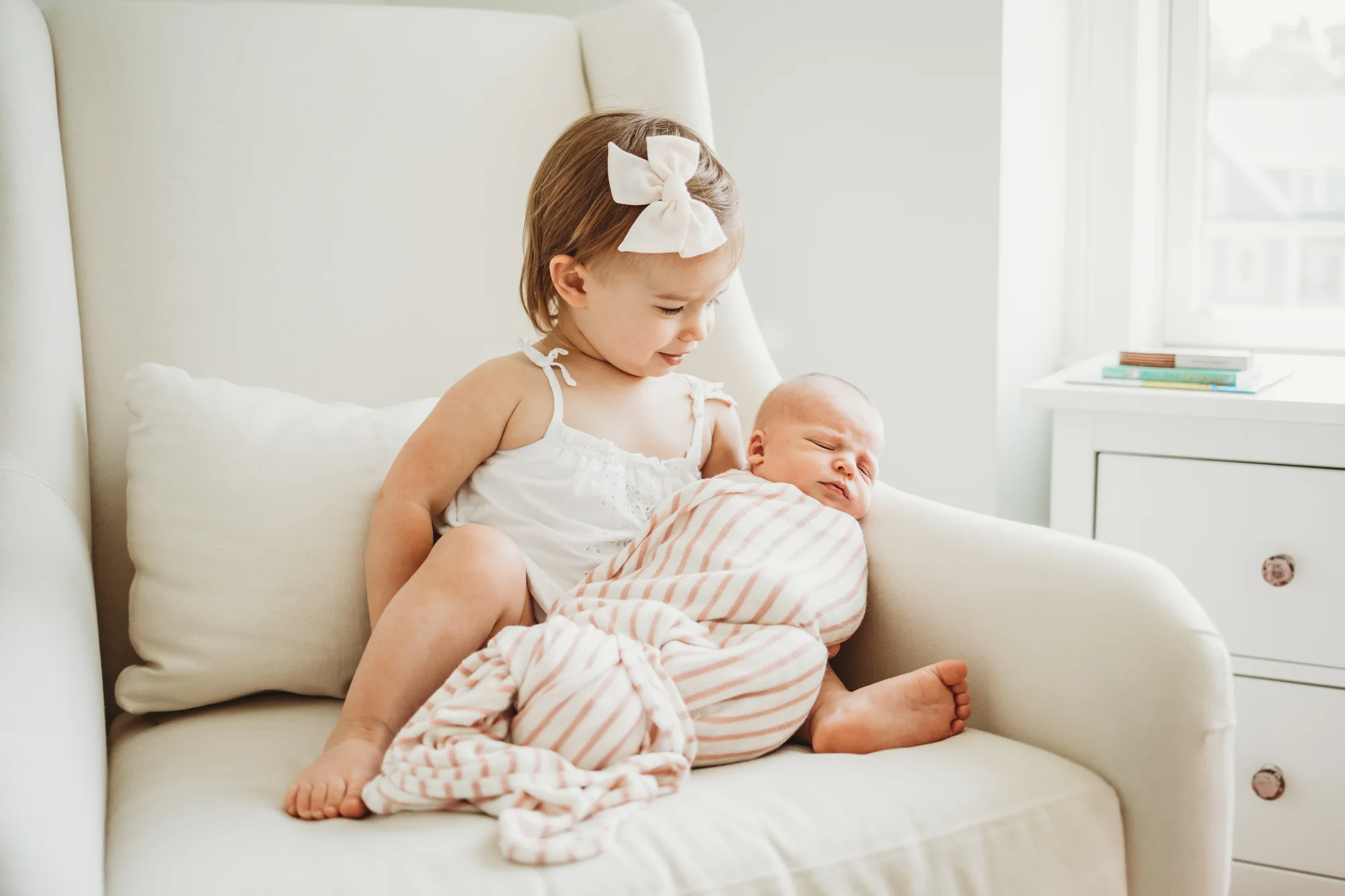 Big sister holding newborn baby sister in a rocker in Wayland, Massachusetts. Wayland family photographer Joy LeDuc.