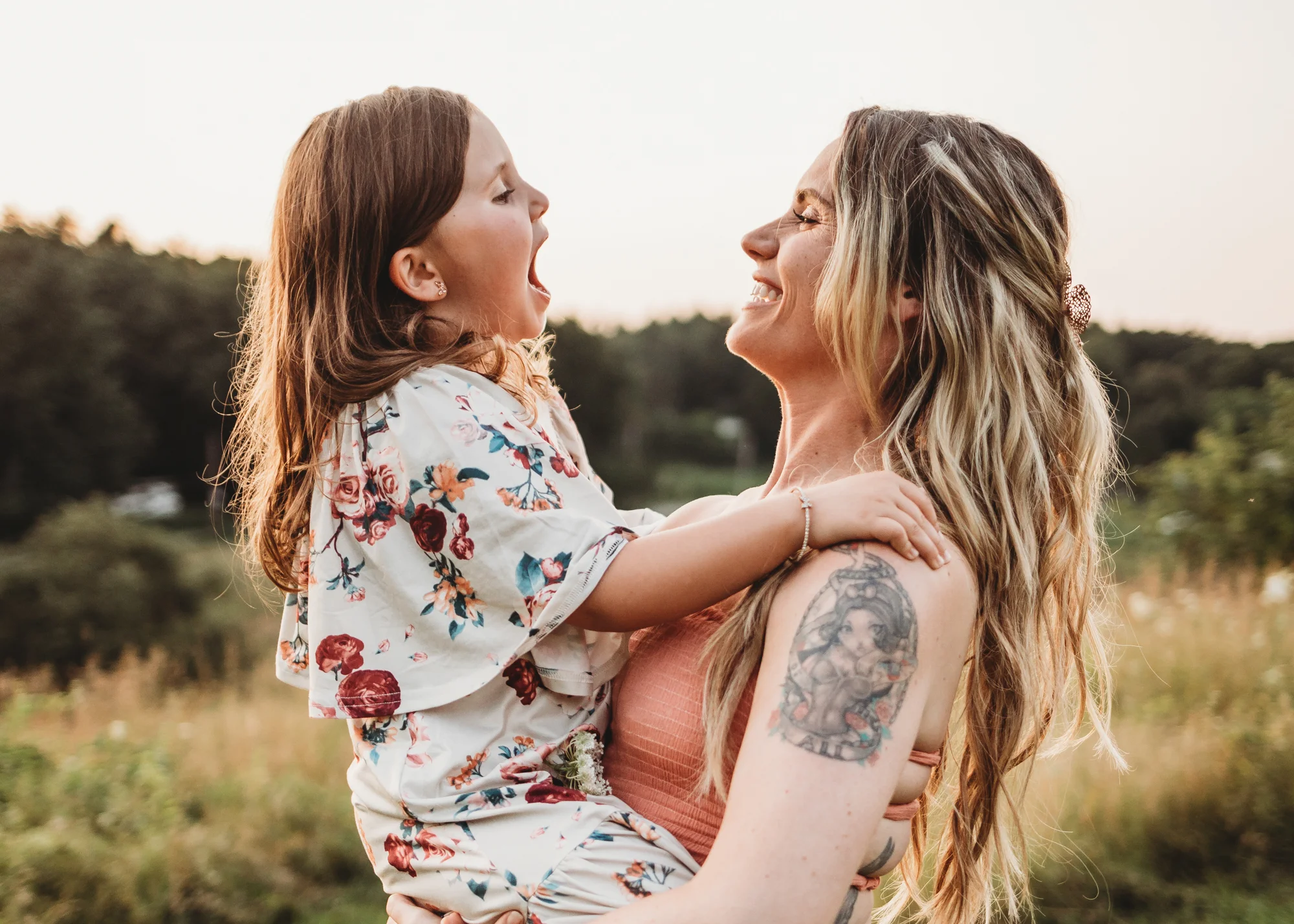Five year old talking with her mouth wide open while mom laughs, holding her. Boho family photography session in Framingham, Massachusetts.