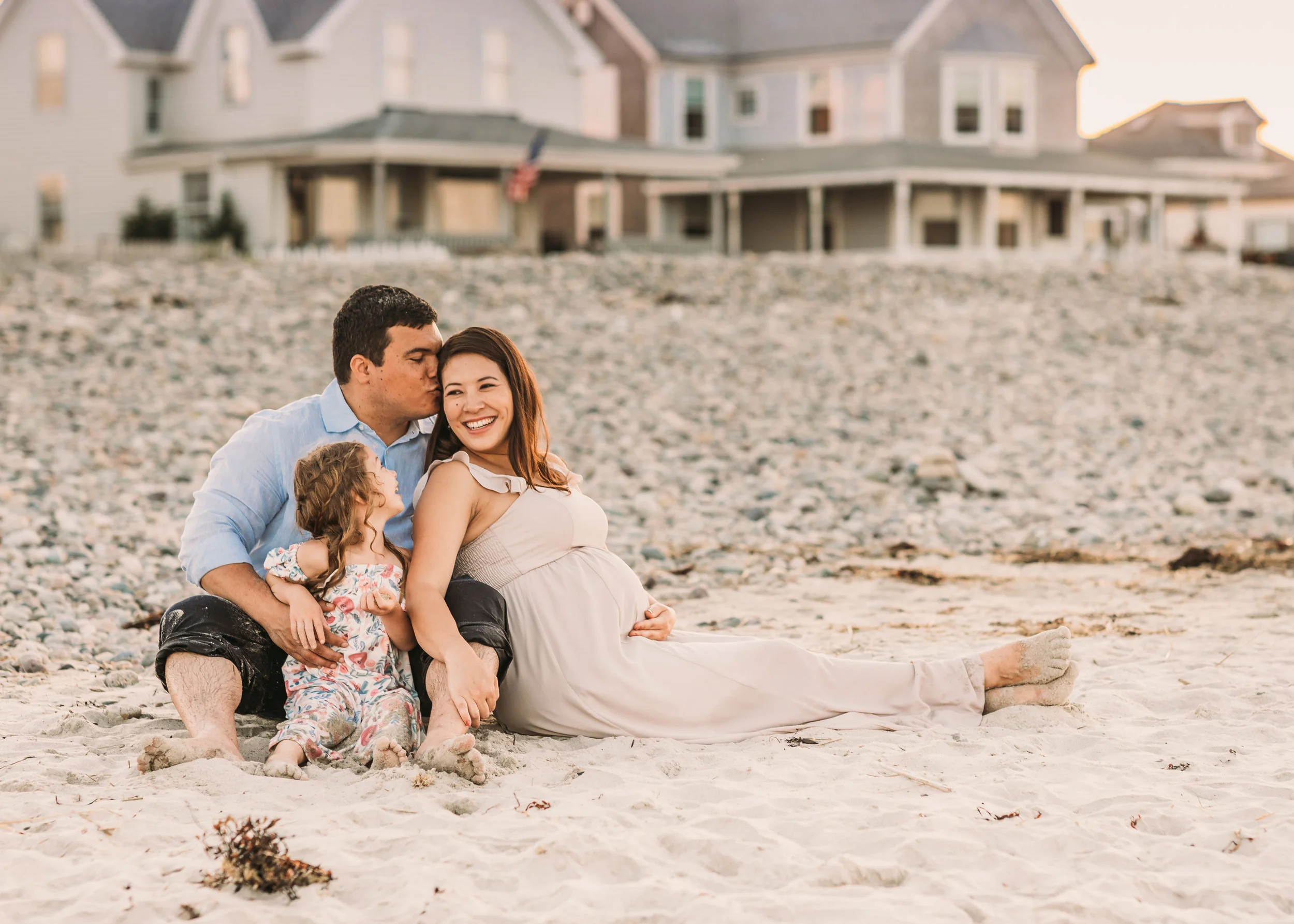 Greater Boston family sitting on the beach in beautiful neutral colored outfits. Five-year-old daughter is in a printed dress, while parents are in solids.