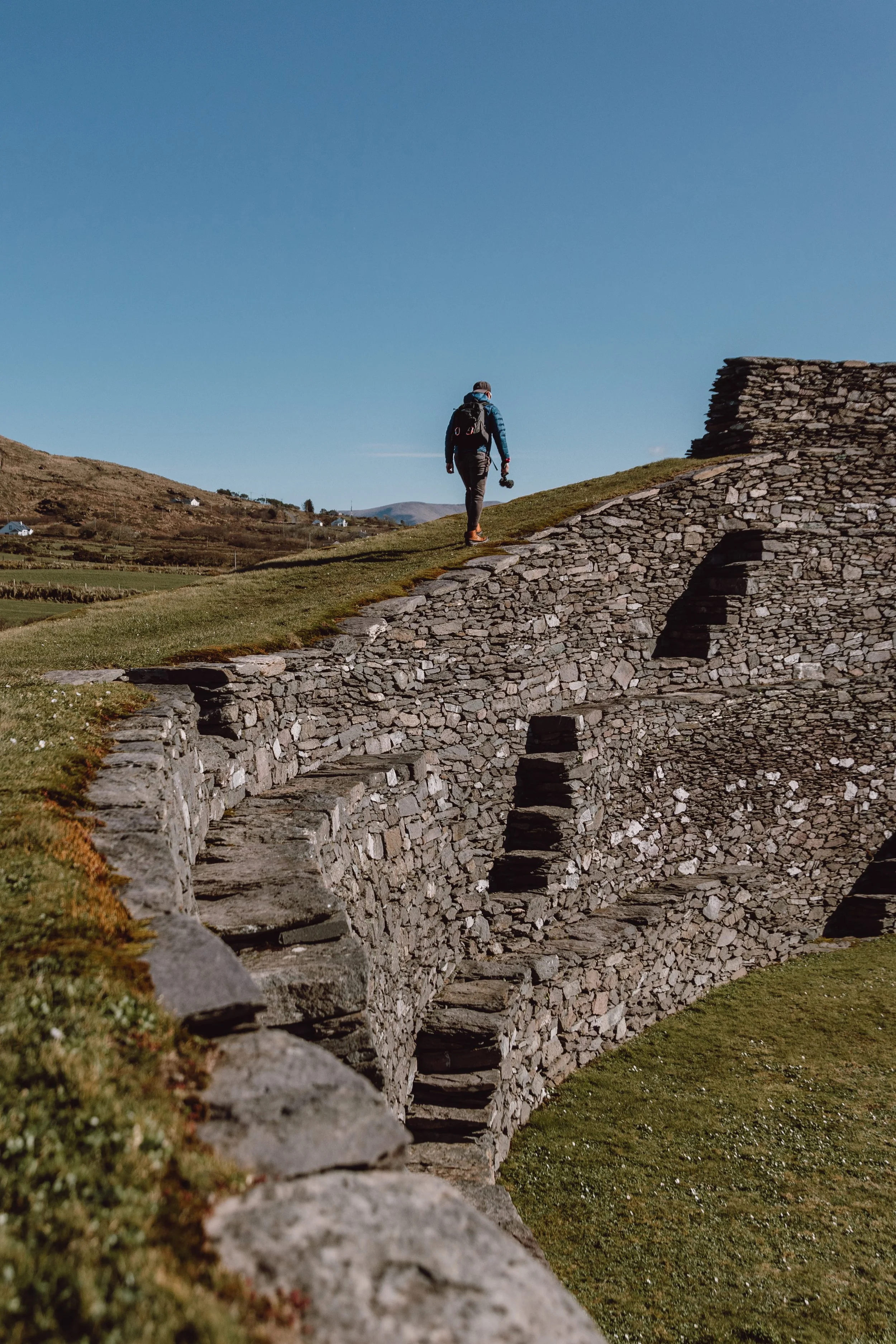 Man walking above Cahergal Stone Fort with clear blue skies