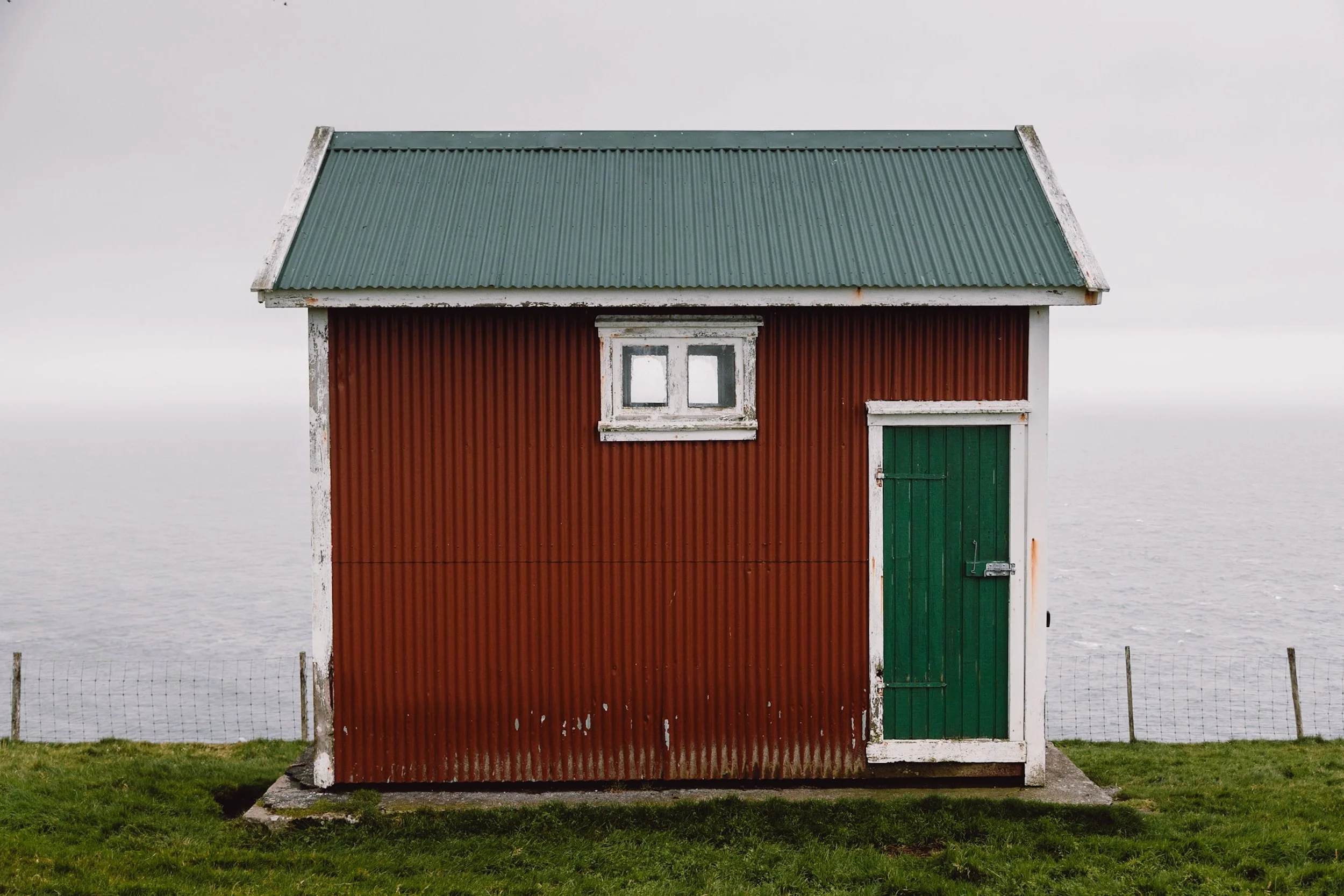 red building against the ocean with green door and red painted walls