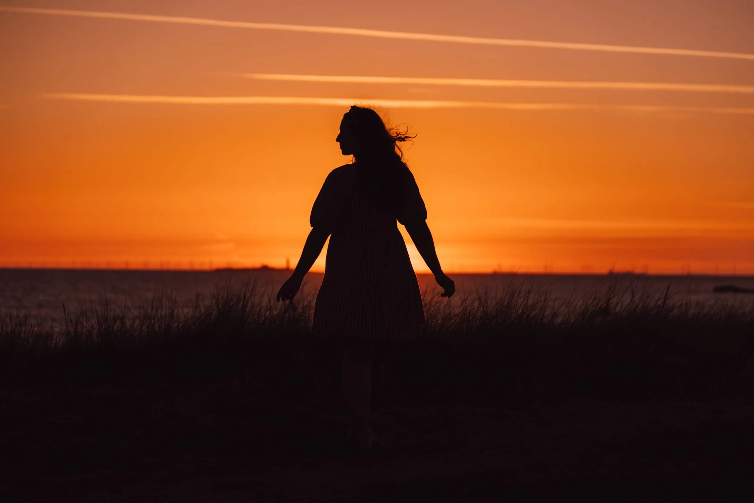 woman standing infront of an orange sky at sunset