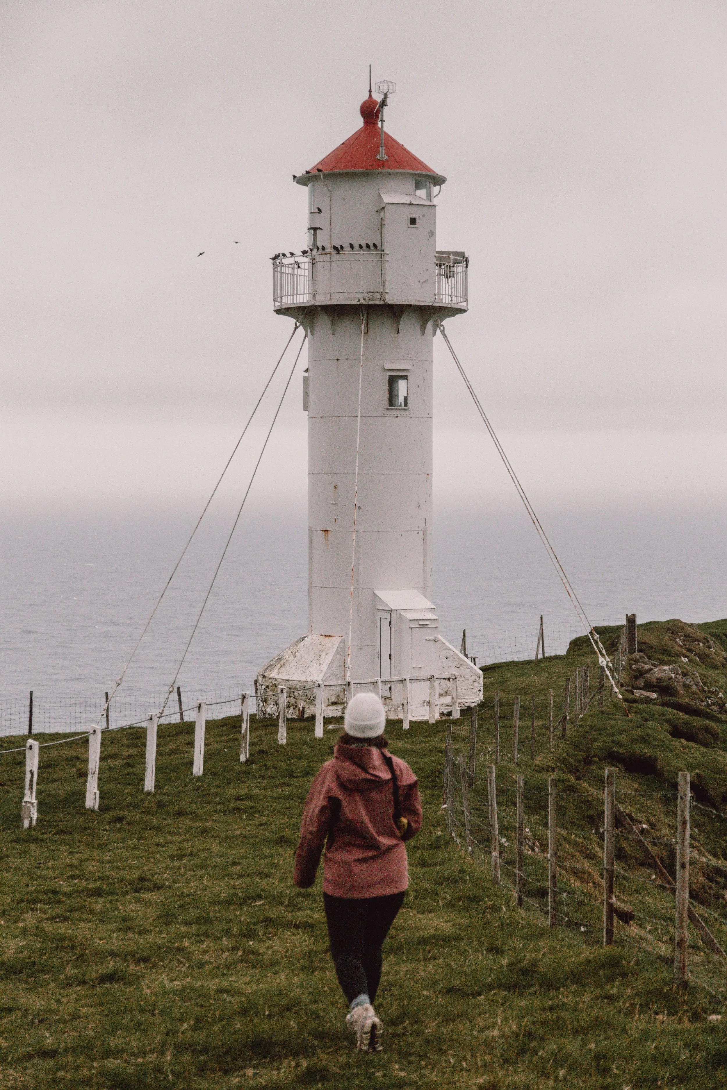 woman walking towards white lighthouse with red roof at Arkberg in Suduroy