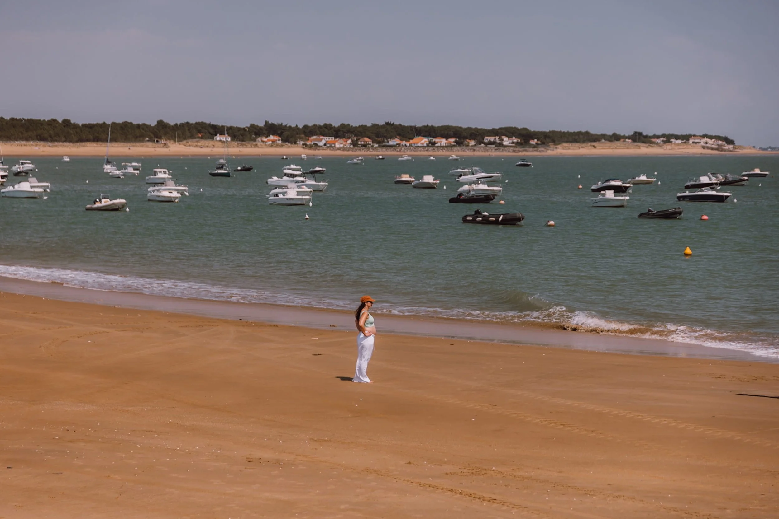 woman standing on sandy beach with boats in the background
