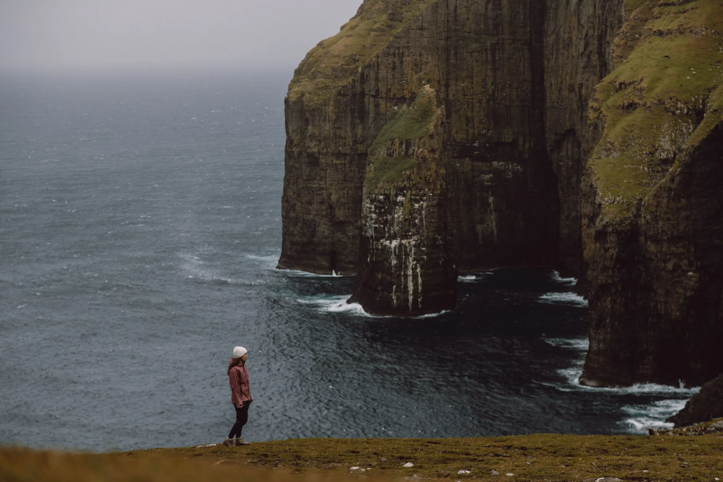 incredible dramatic scenery of cliffs and stacks with woman standing foreground at Ásmundarstakkur Sea Stack
