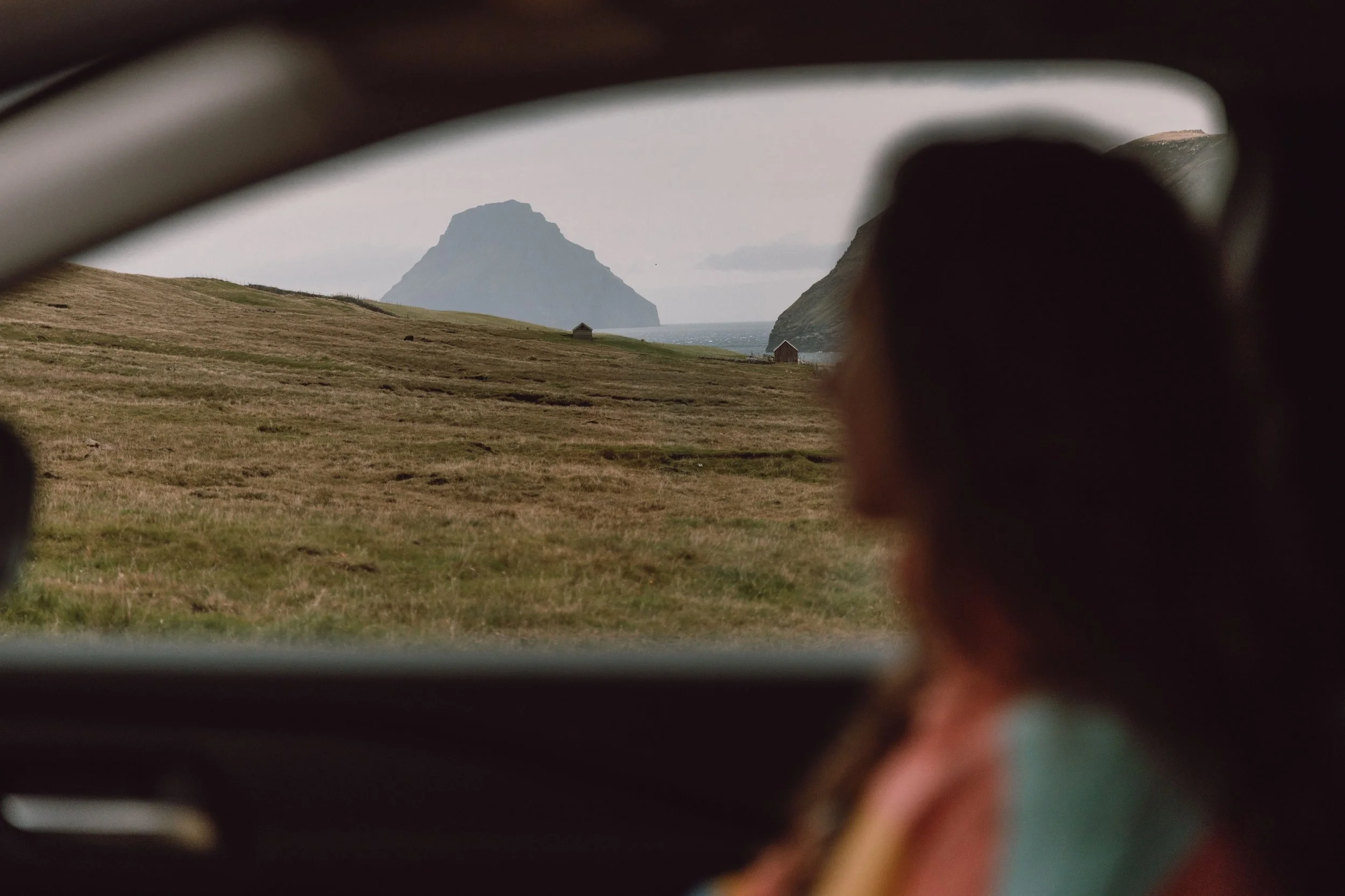 woman silhouette sat in a car looking over to island in suduroy