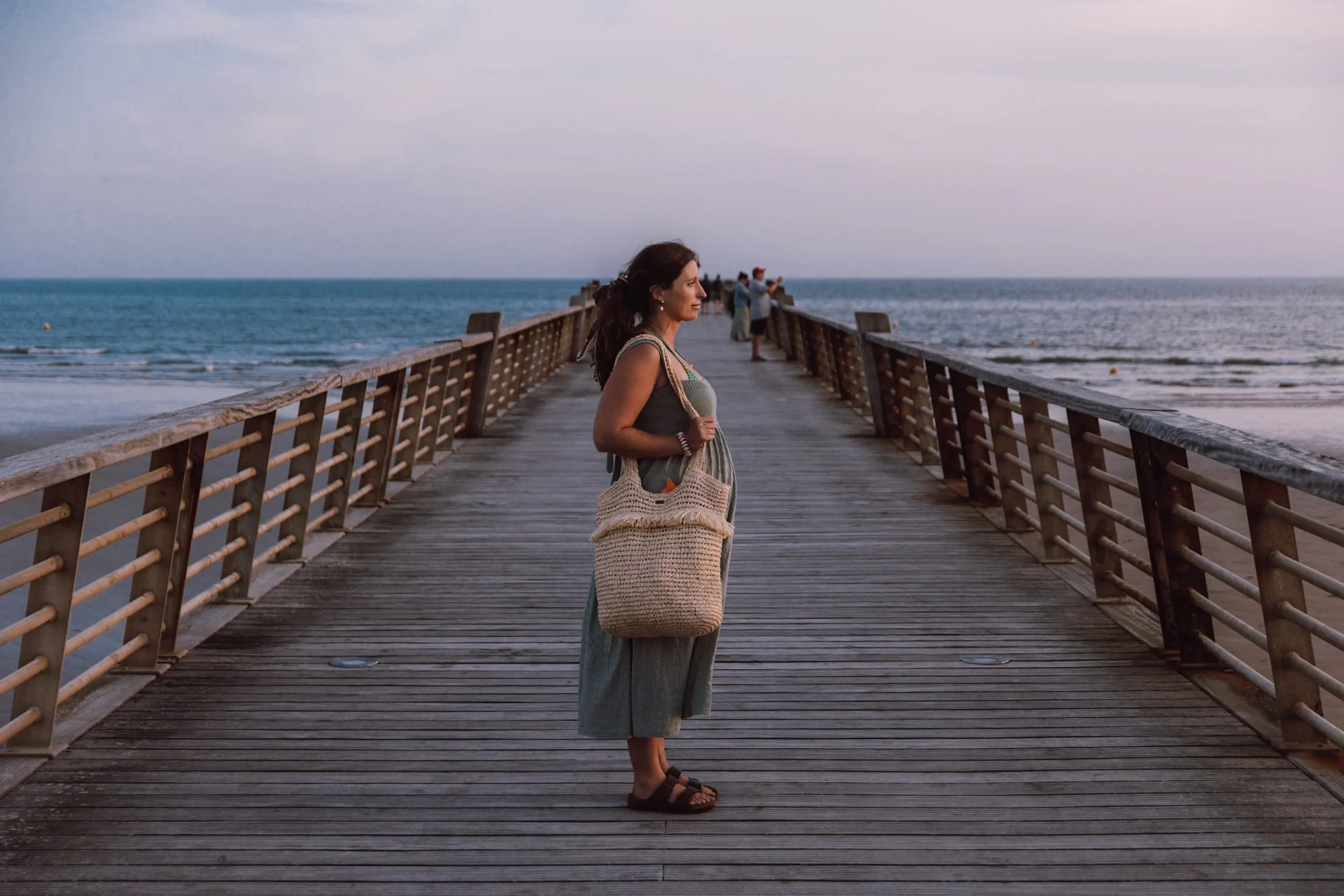 woman standing on wooden boardwalk at sunset