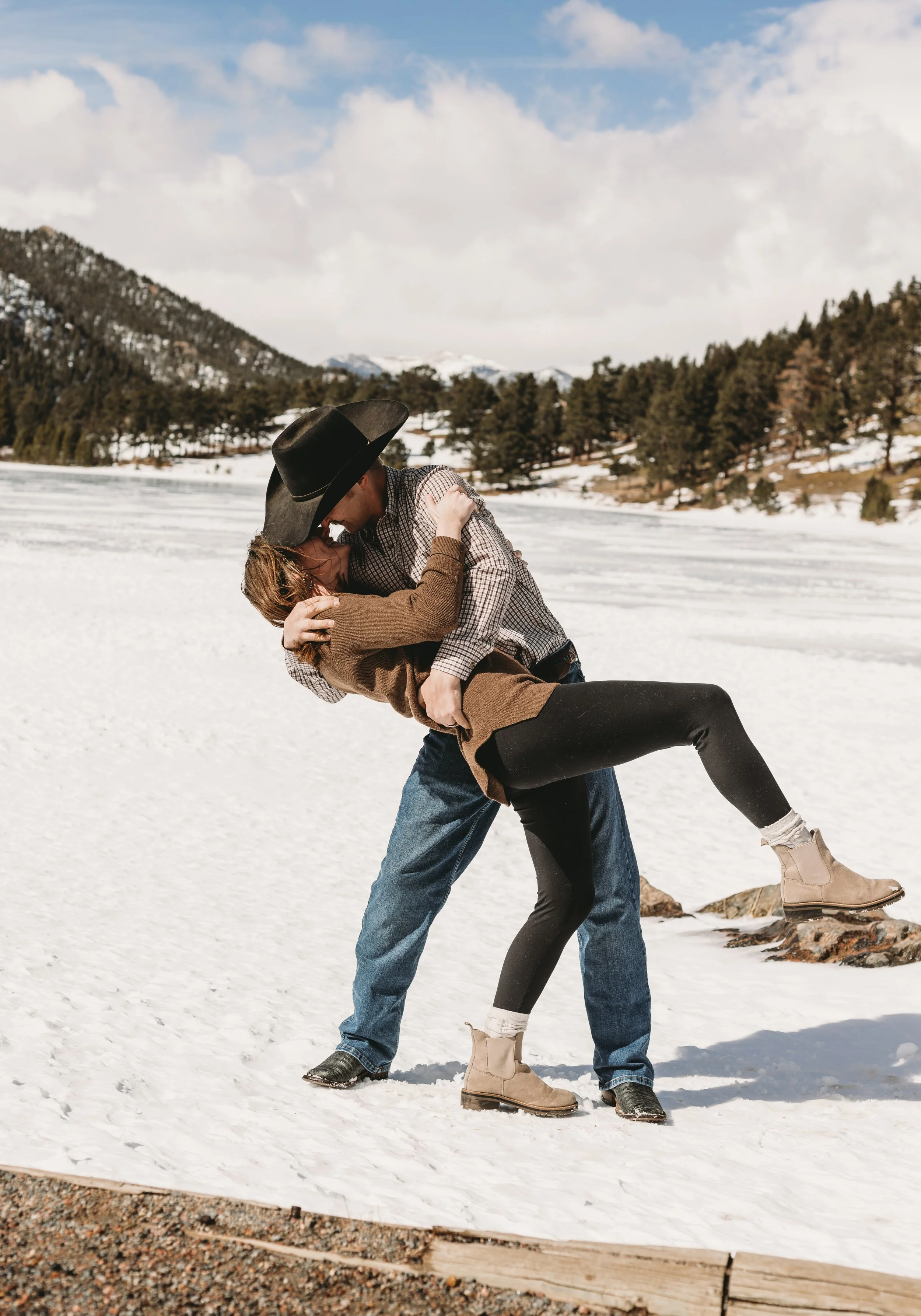 A couple dancing on a snowy landscape with mountains and trees in the background
