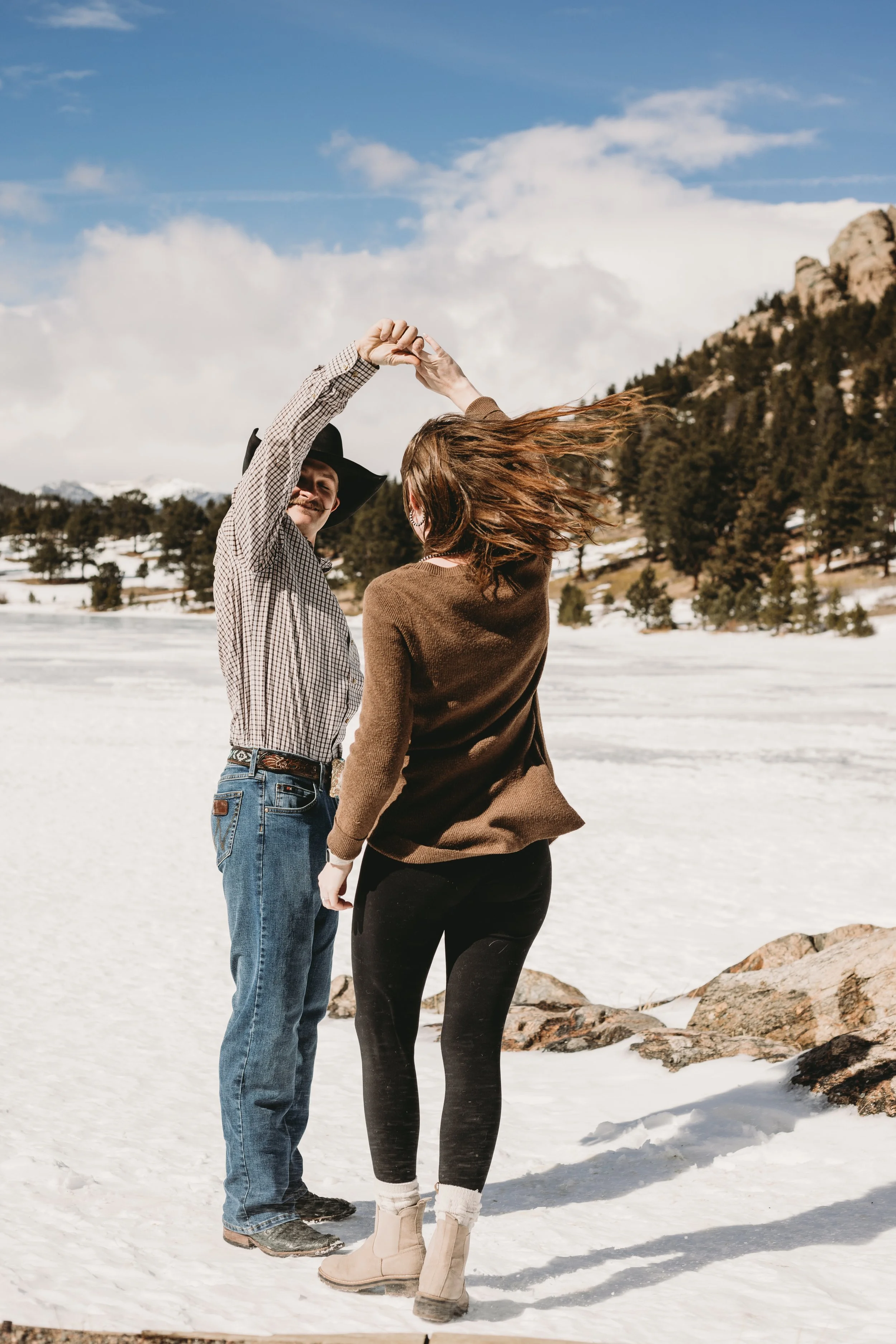 A couple dancing outdoors on a snowy landscape with mountains and trees in the background, holding hands and spinning.