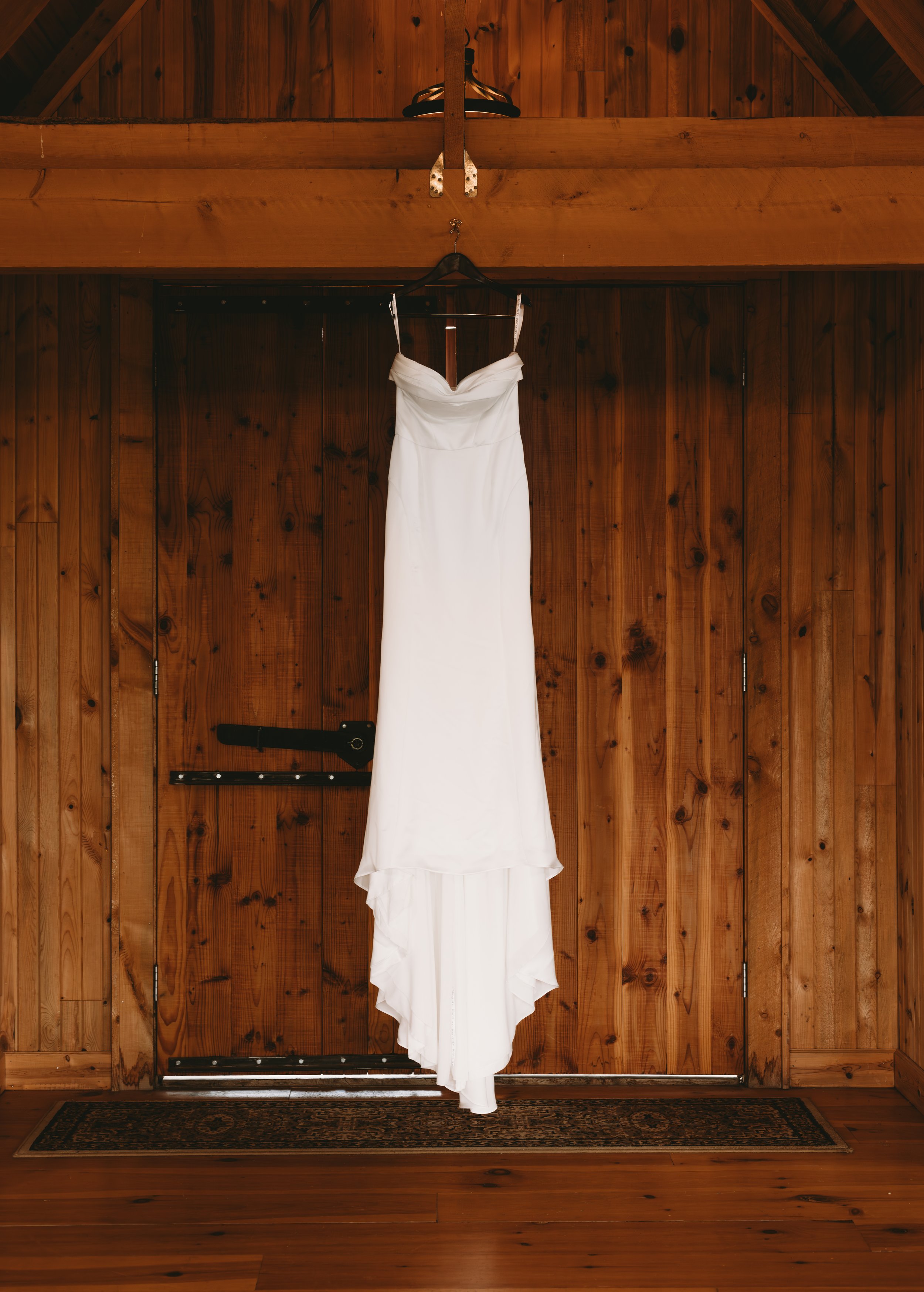 A white wedding dress hanging on a wooden barn door.