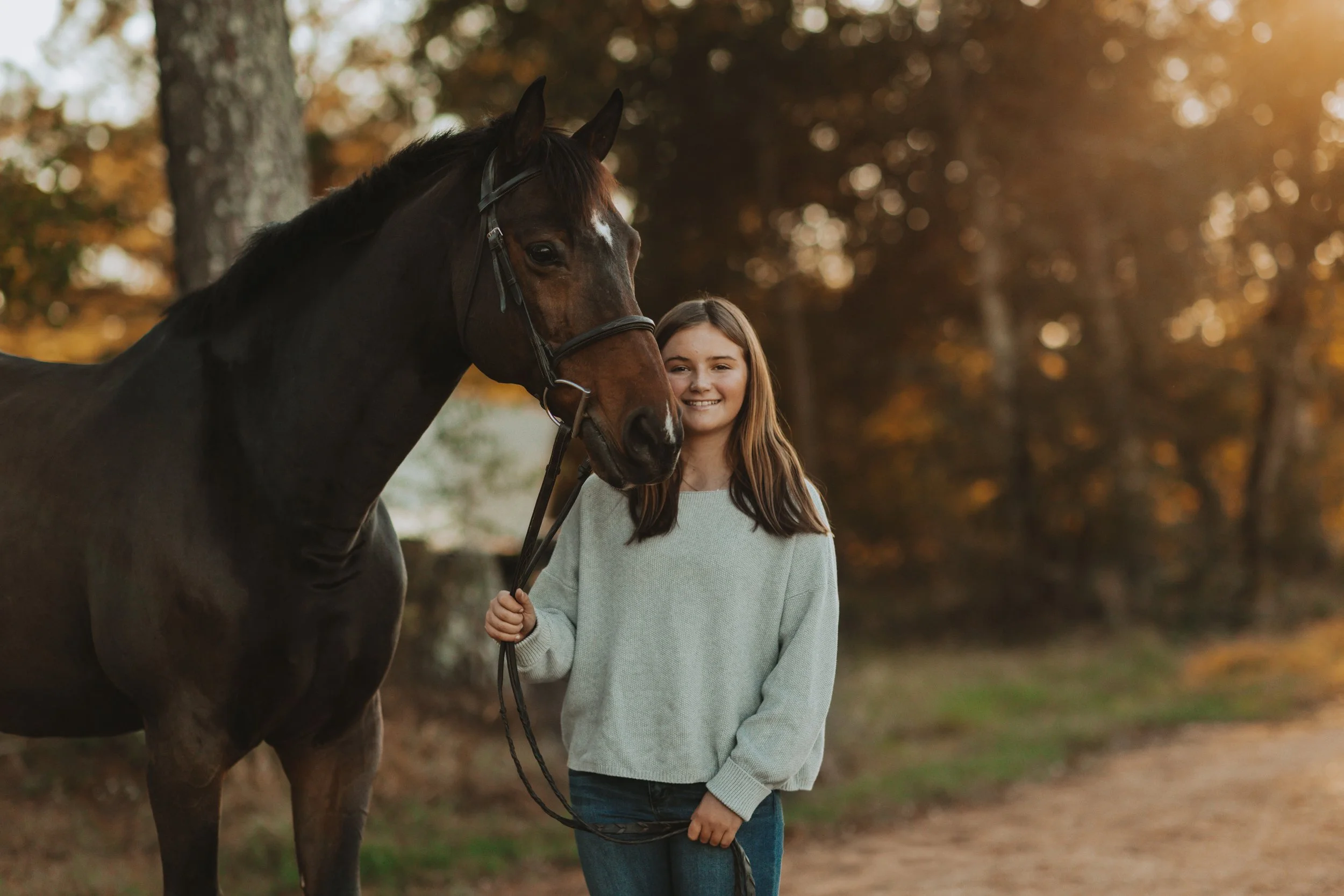 A girl holding a horse's reins outdoors during sunset.