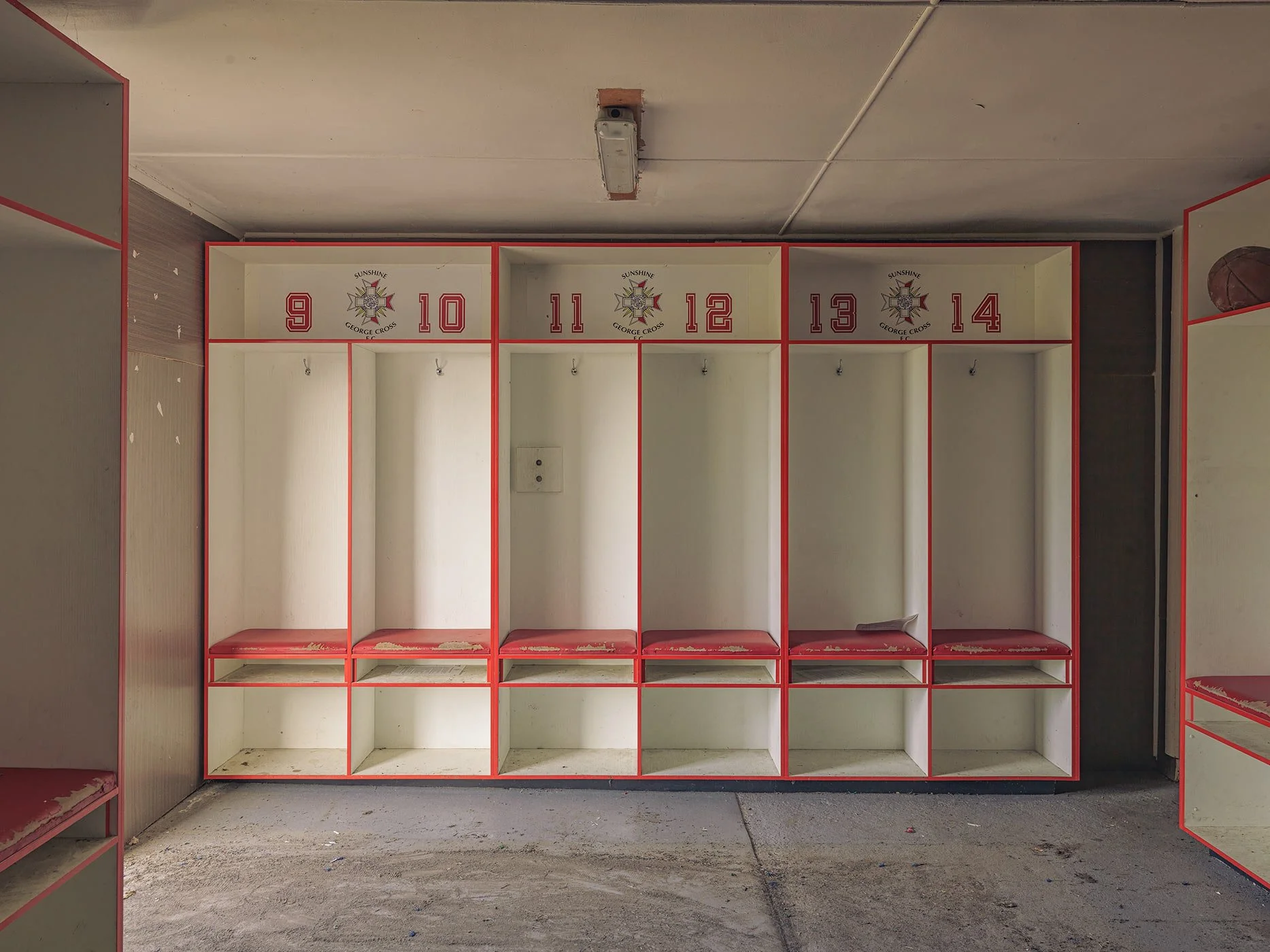 Empty lockers with red borders and numbers from 9 to 14, a football in the upper right corner, and a concrete floor.