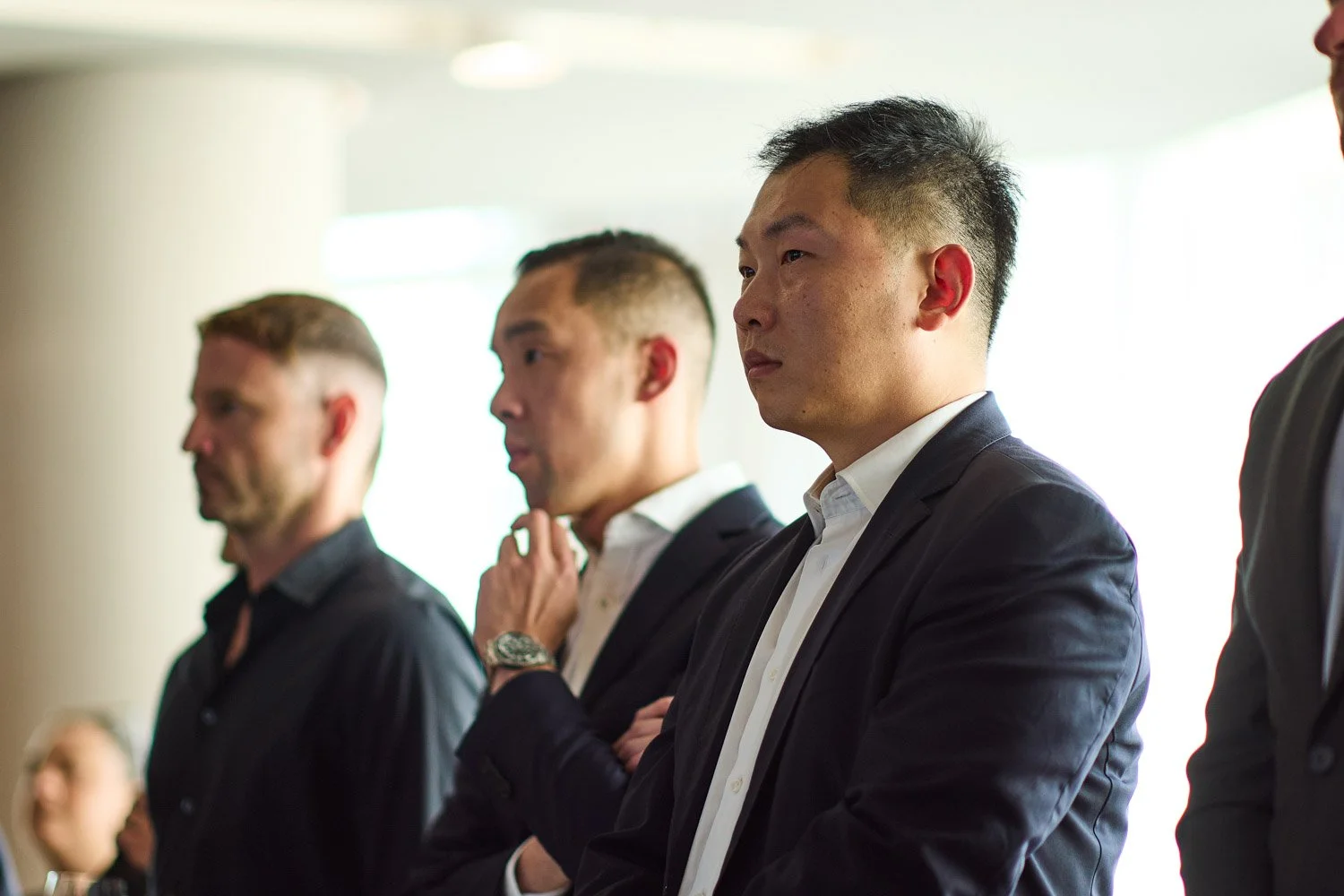 Four men in business attire standing with arms crossed during a meeting or presentation in a well-lit room.