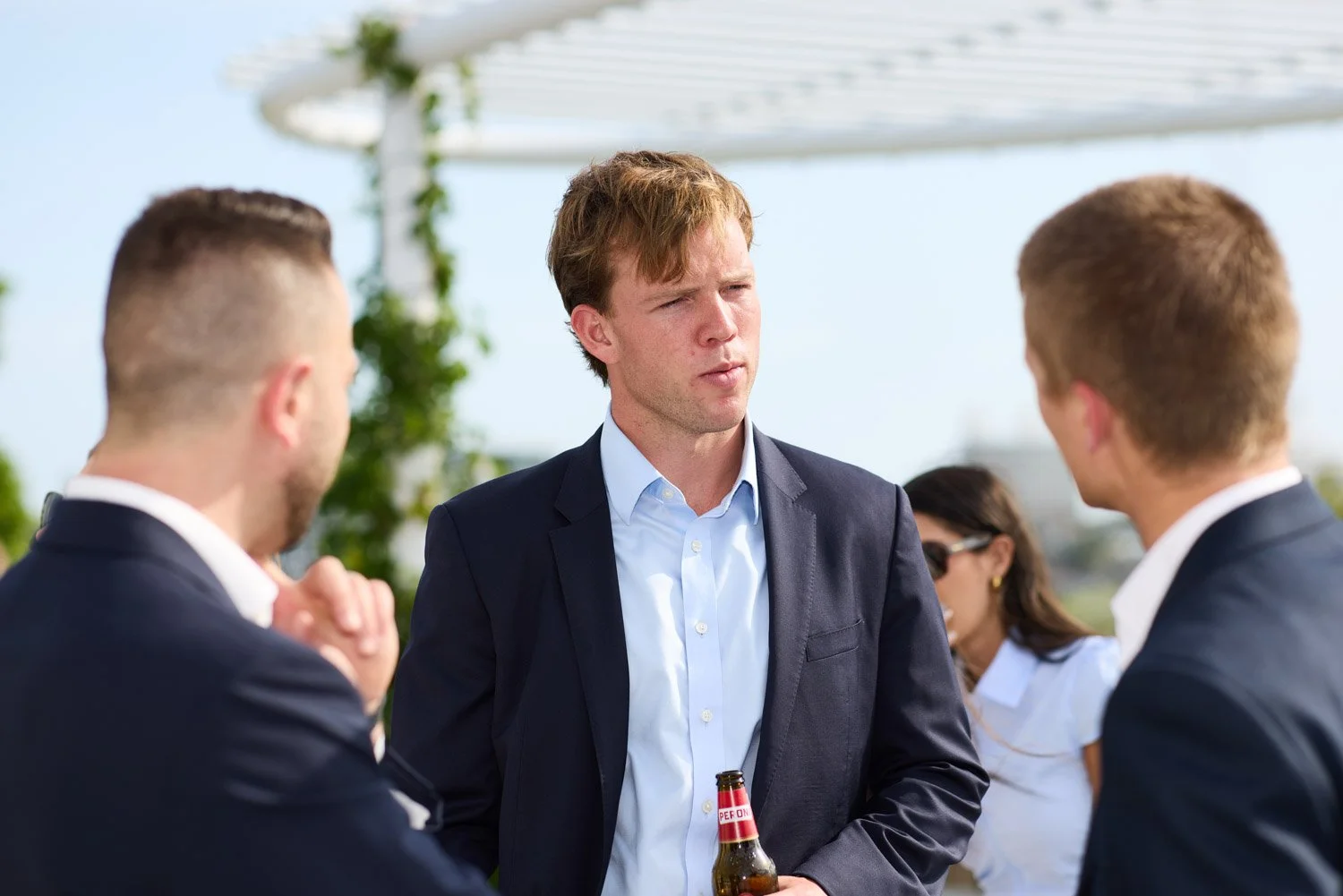 A group of young adults dressed in business attire having a conversation outdoors on a sunny day.