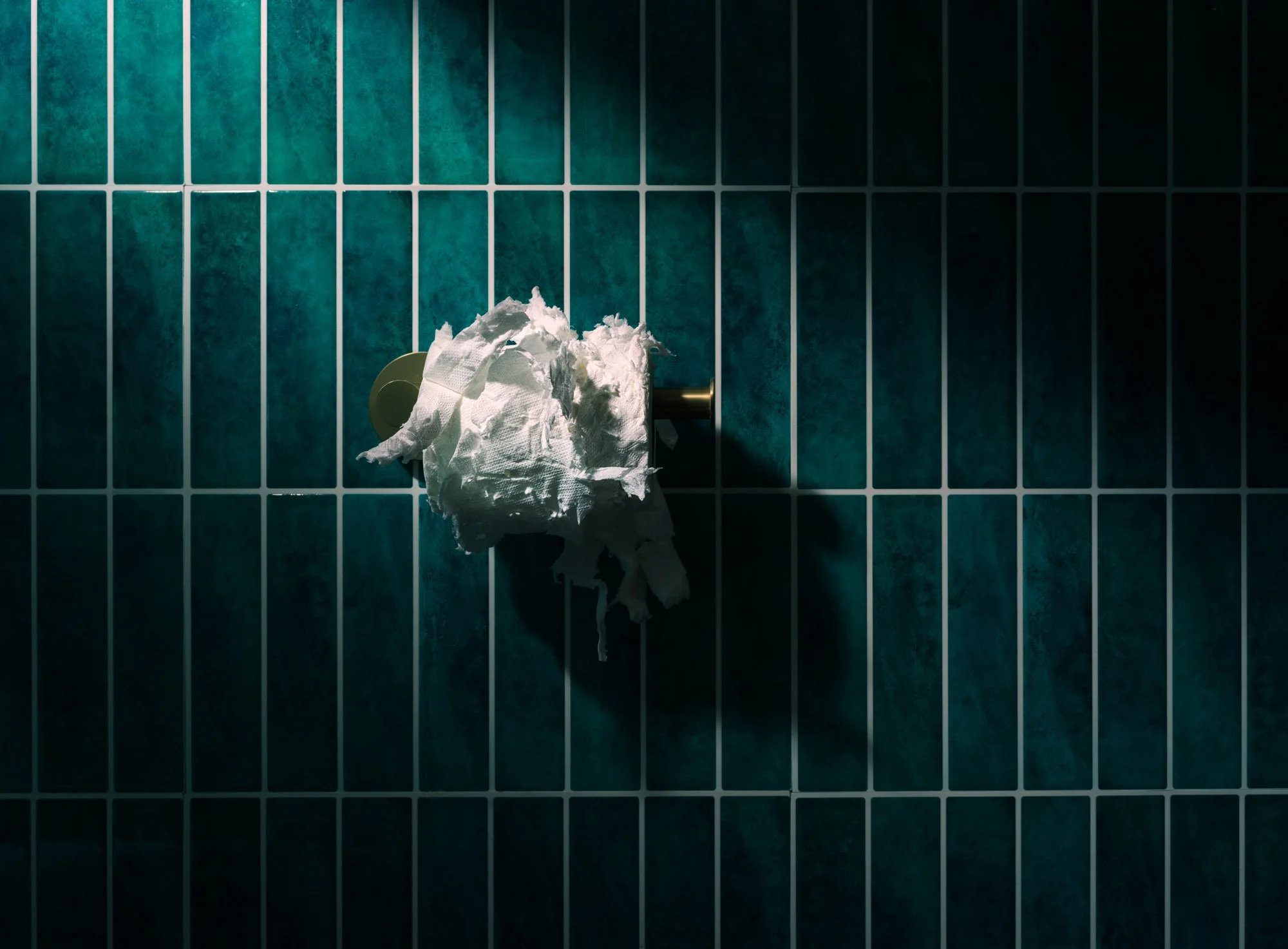 A partially used roll of toilet paper on a metallic holder attached to a wall with teal tiles.