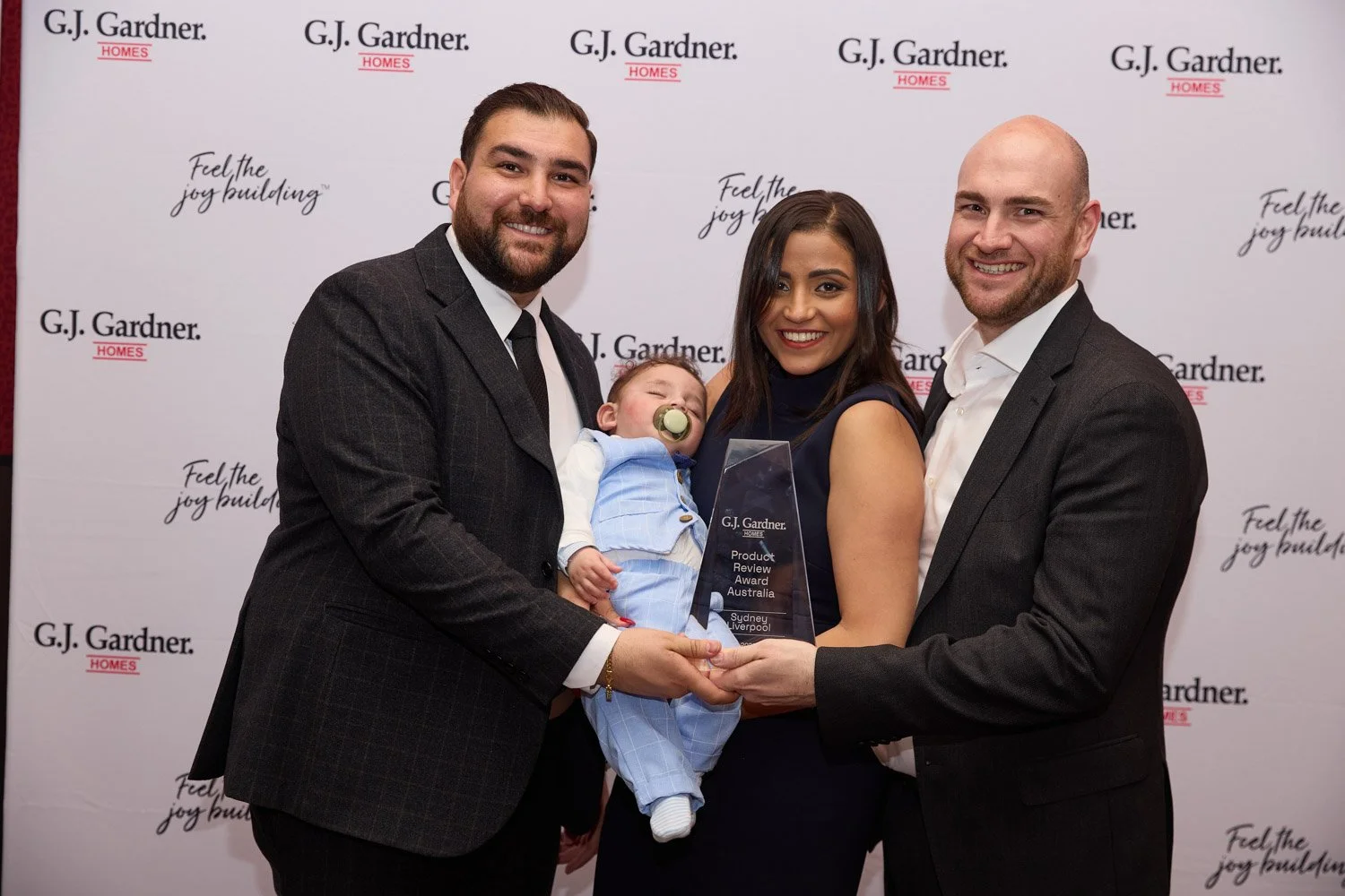 Group of four adults and one baby at an award ceremony, holding a G.J. Gardner Homes product review award.
