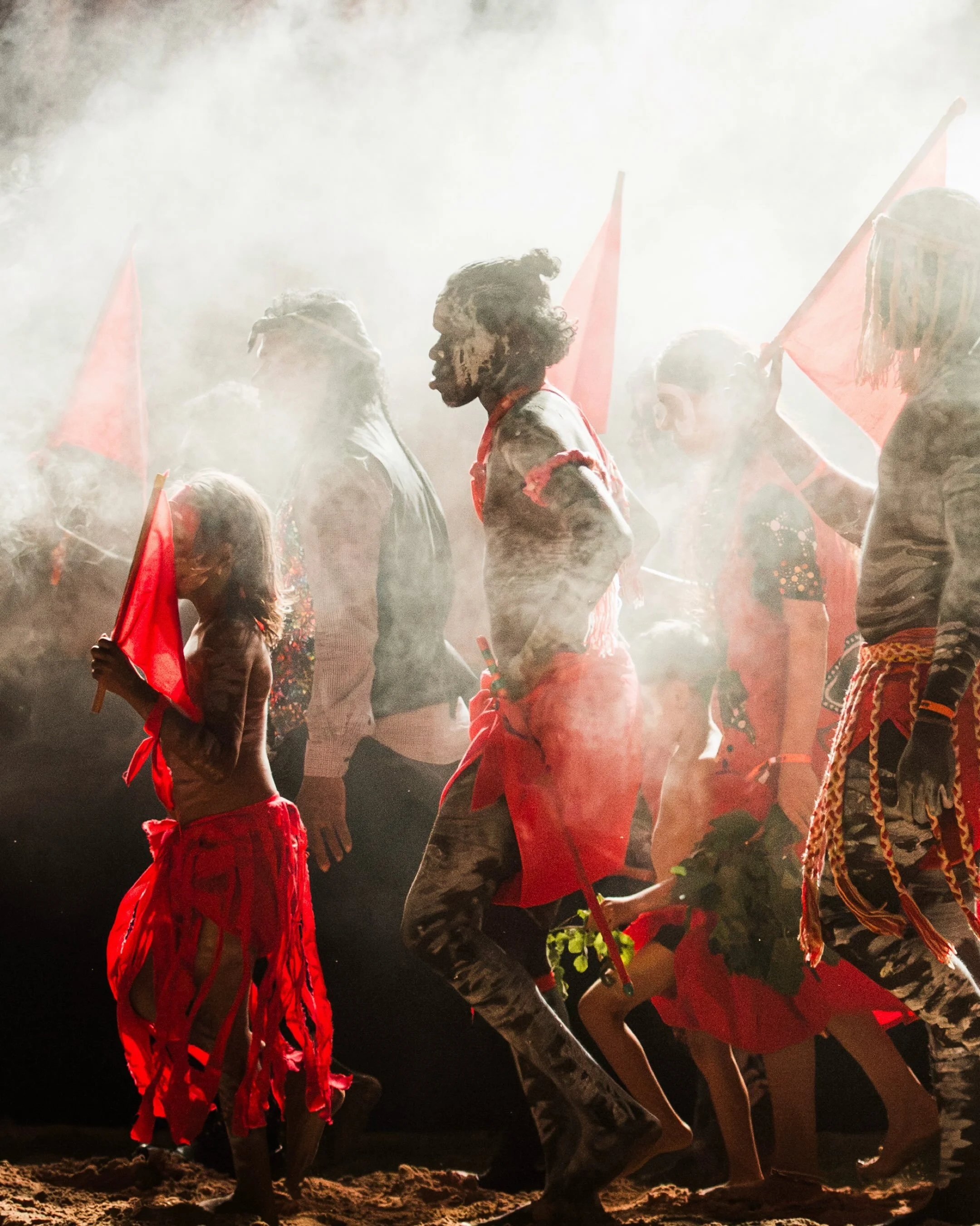 Smoke and paperbark, ochre and sand; the sound of feet stamping the earth as the yidaki drones through the night air. The Red Flag Dancers of Numbulwar dancing their story on Larrakia Country.