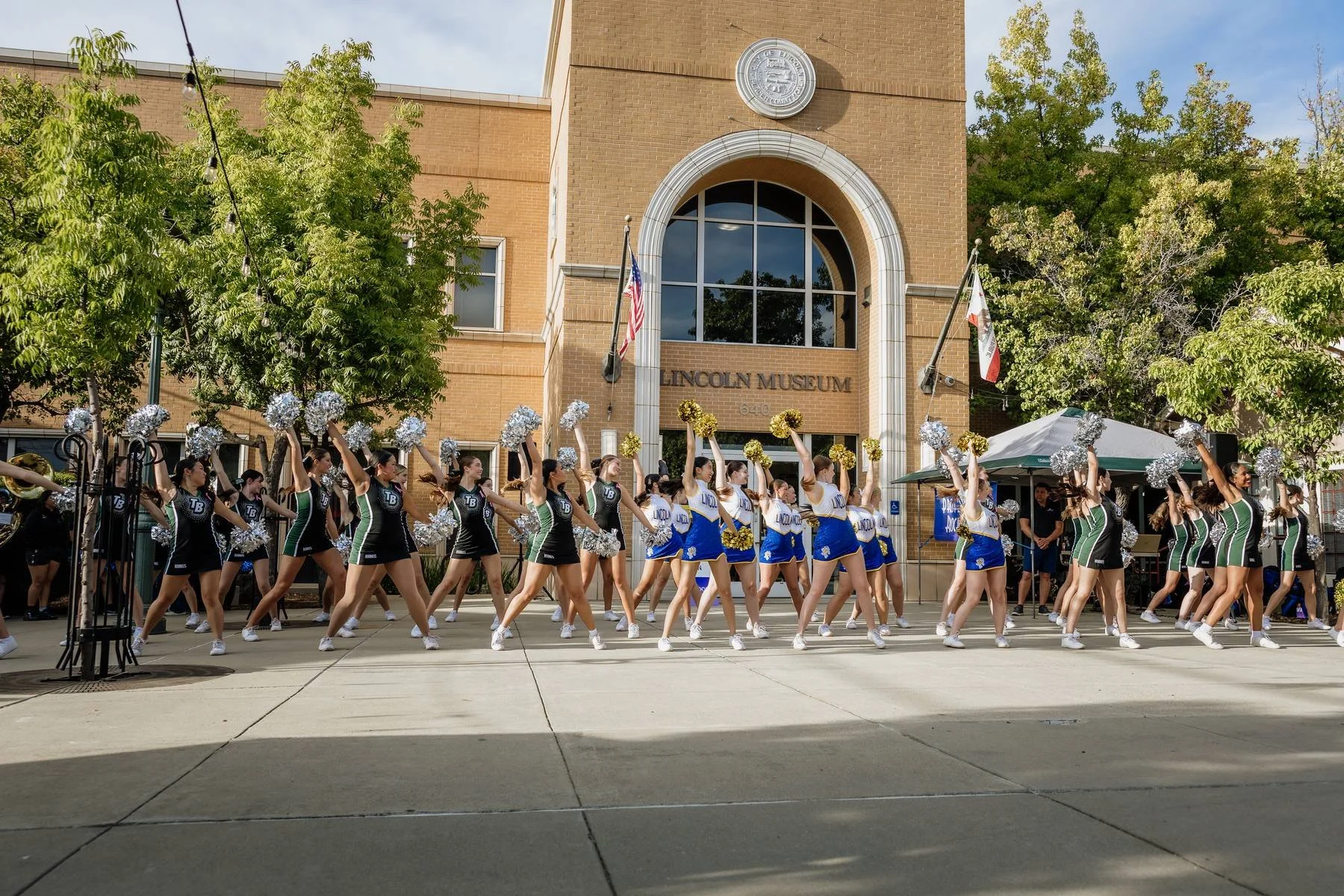 Cheerleading team performing outside Lincoln Museum, with cheerleaders holding pom-poms and dressed in green, black, white, and blue uniforms.